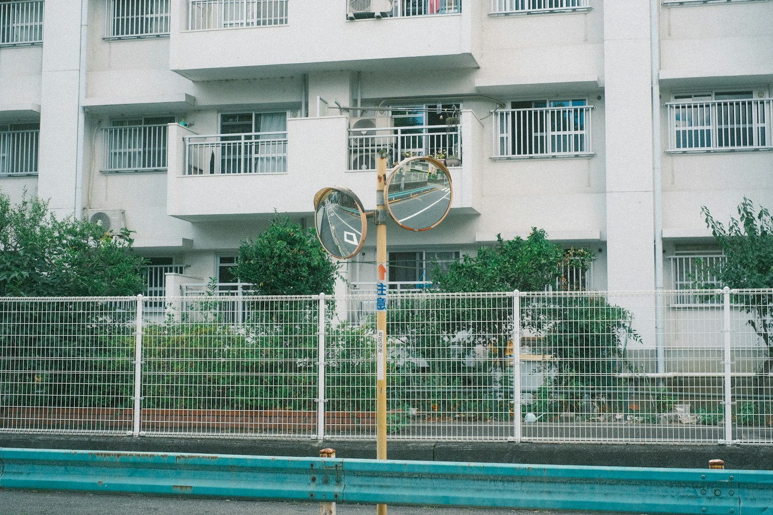 Two mirrors in front of a white building and a fence