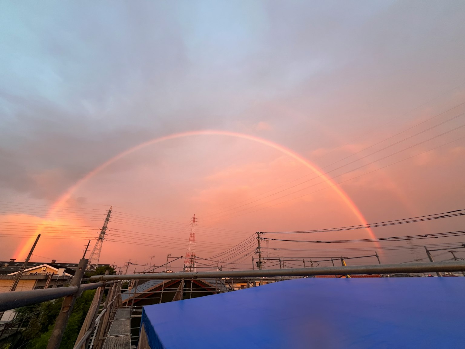 夕焼けの空に大きな虹がかかる風景 鉄塔と電線が見える