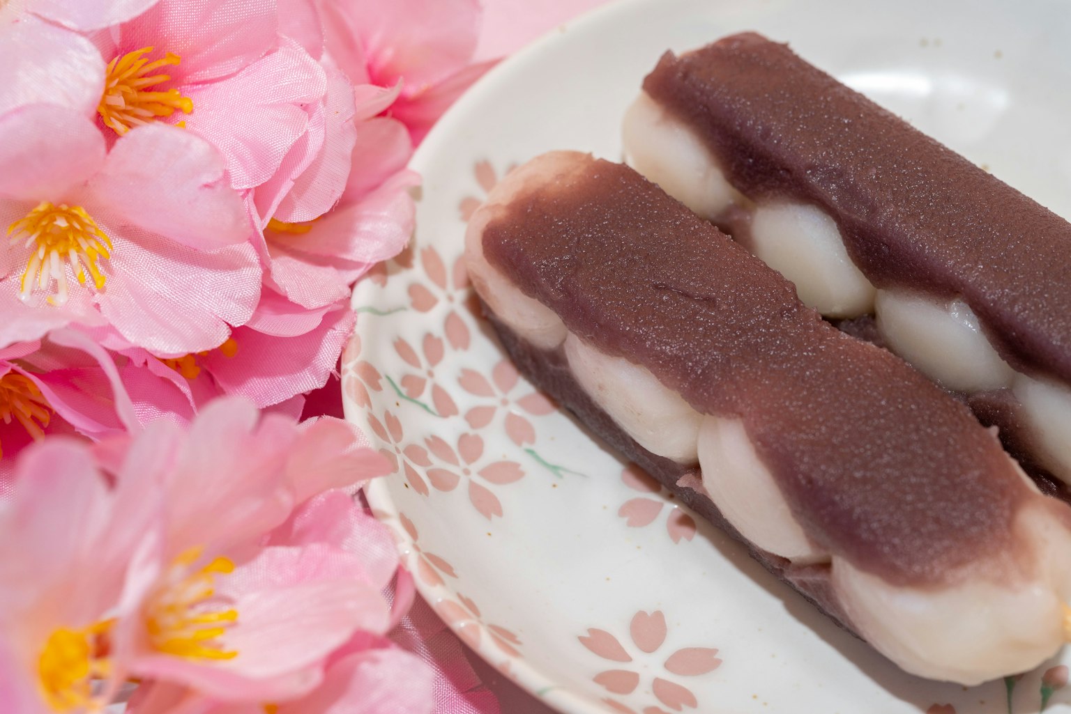 Un piatto di dolci giapponesi con due pezzi di pasta di fagioli rossi accanto a fiori di ciliegio rosa