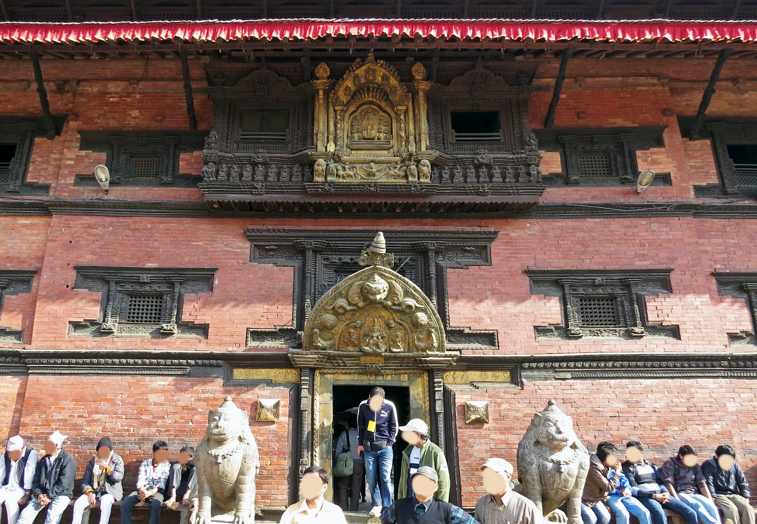 Des gens assis devant un bâtiment traditionnel népalais avec des sculptures de lions