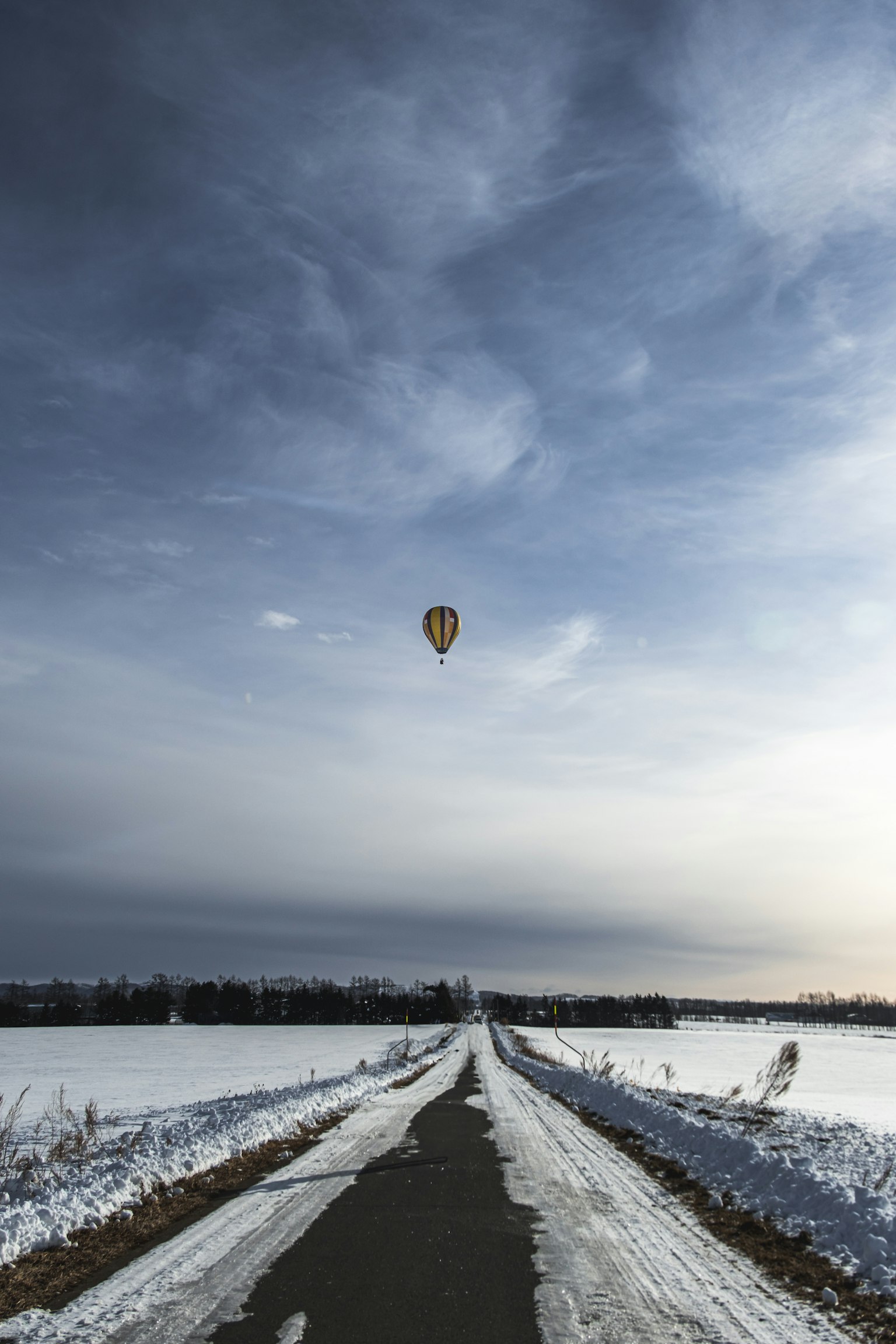 A snowy road leading towards a hot air balloon in the sky