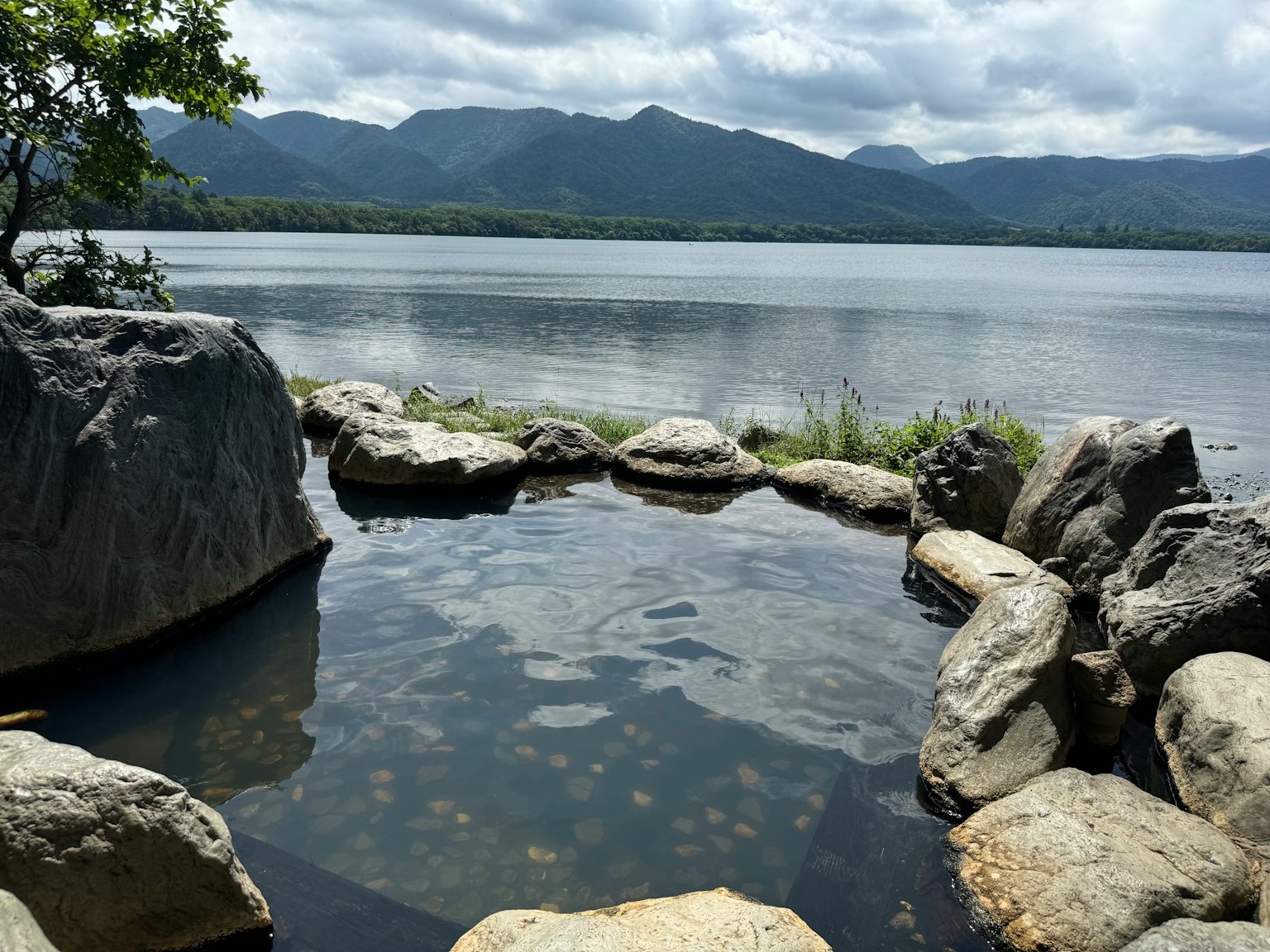 Pemandian air panas alami di dekat danau yang tenang dikelilingi batu
