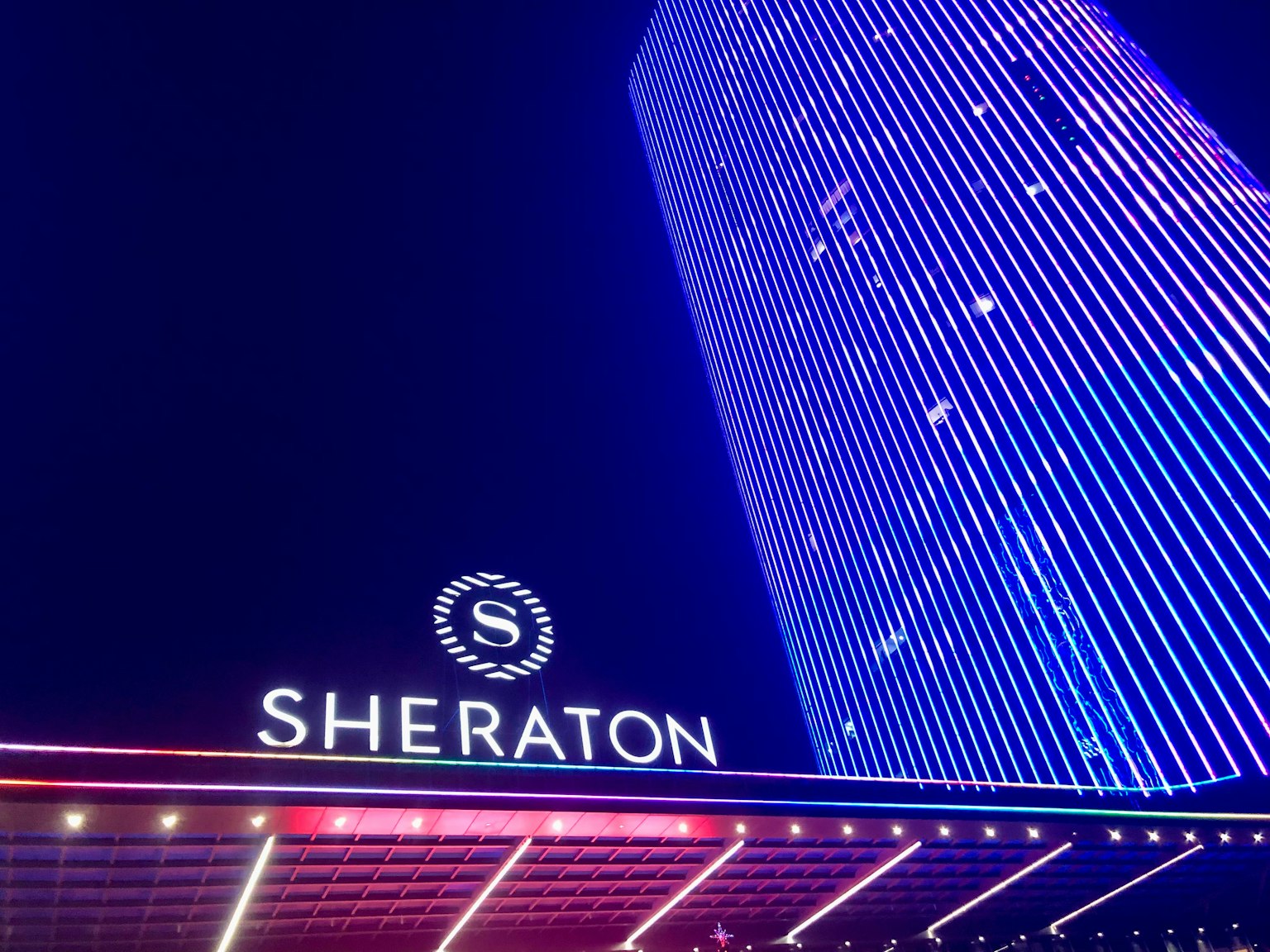 Vista esterna dell'hotel Sheraton illuminato con luci blu e viola di notte