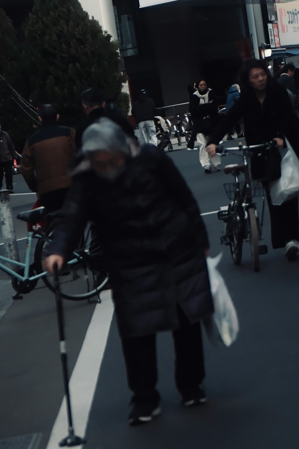 街中で杖をついて歩く高齢者と自転車の通行人がいる風景