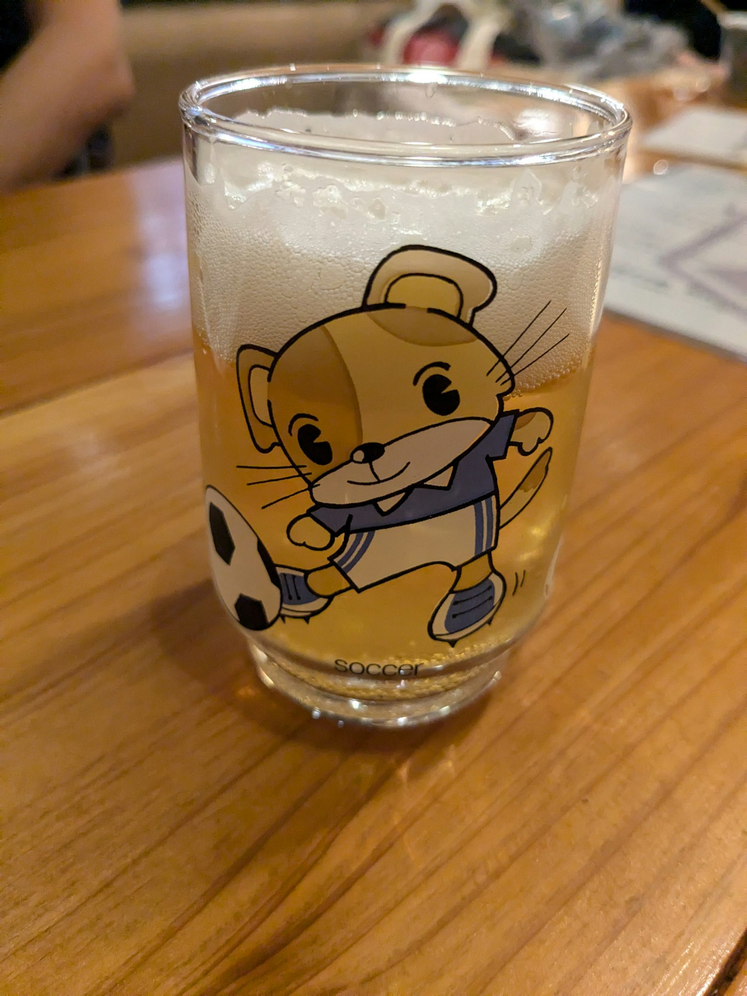 A clear glass of beer featuring a cute character playing soccer