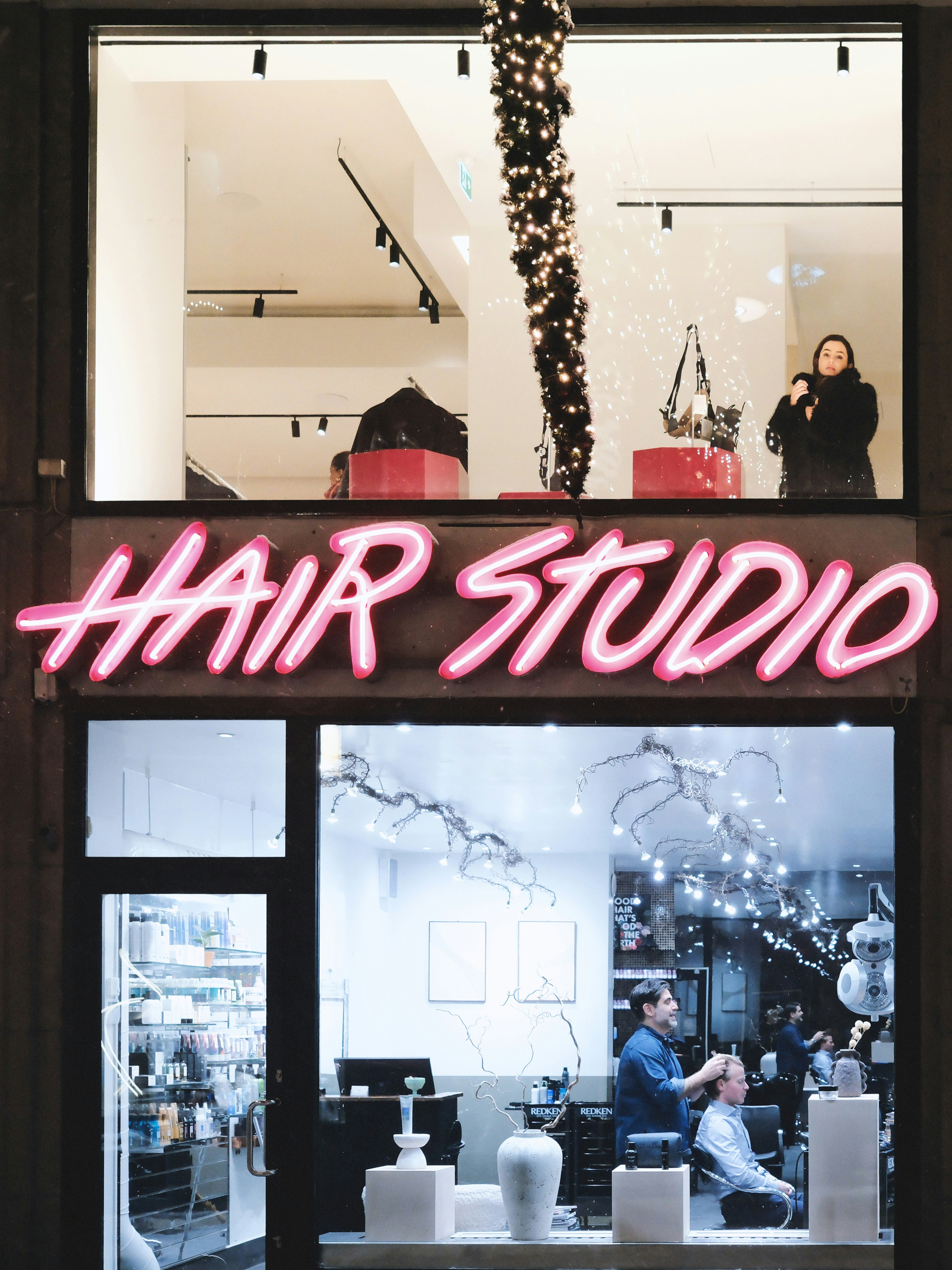 ガラス越しに見える人々と「HAIR STUDIO」のネオン看板のある店内