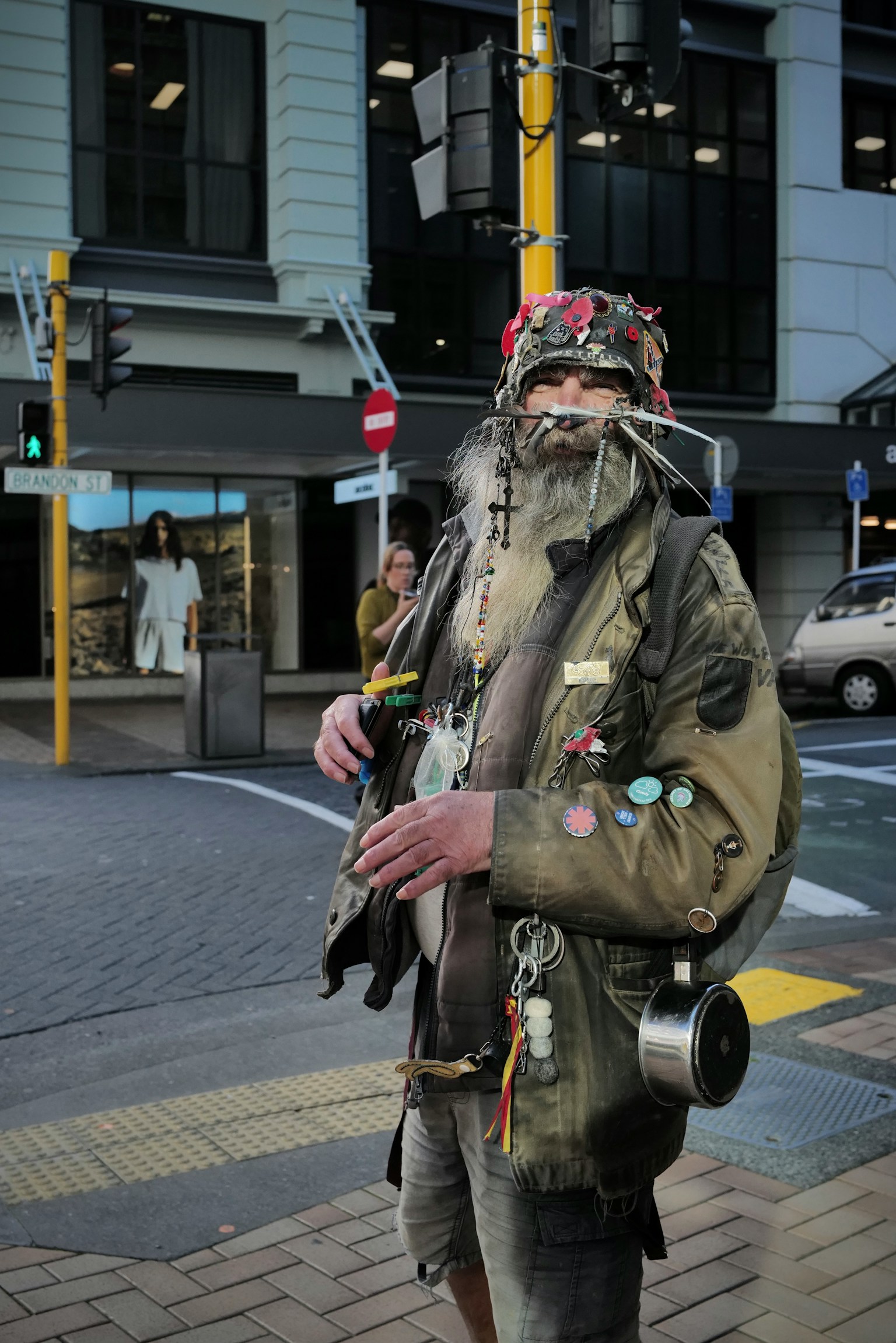 A unique man standing on a street corner wearing a decorated jacket with various badges
