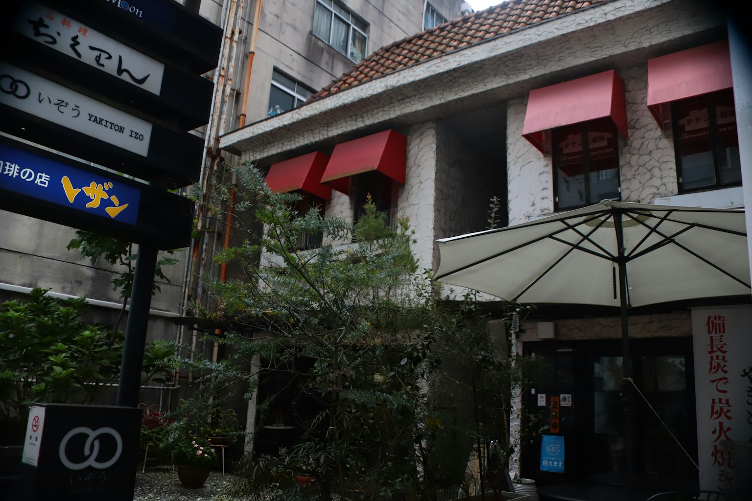 Exterior de un restaurante con toldos rojos rodeado de vegetación