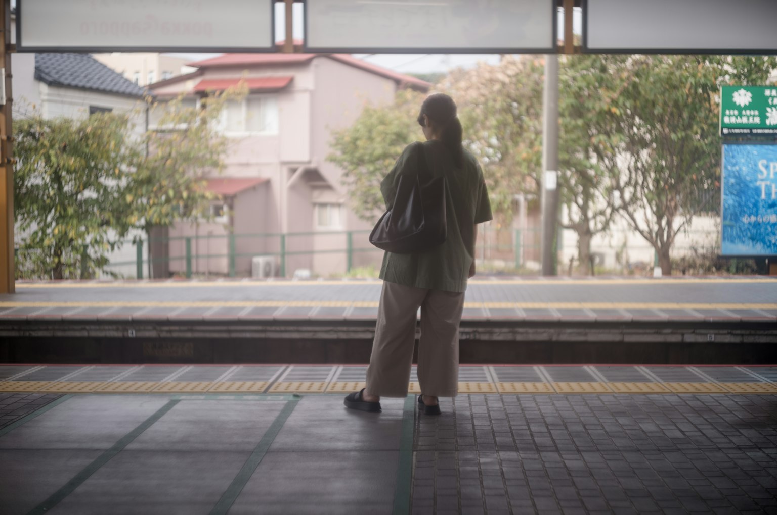 Femme attendant sur le quai de la gare entourée d'arbres et de maisons