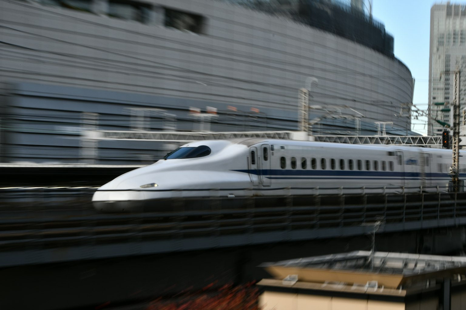 Tàu Shinkansen đang chạy nhanh trên đường ray với các tòa nhà thành phố ở nền
