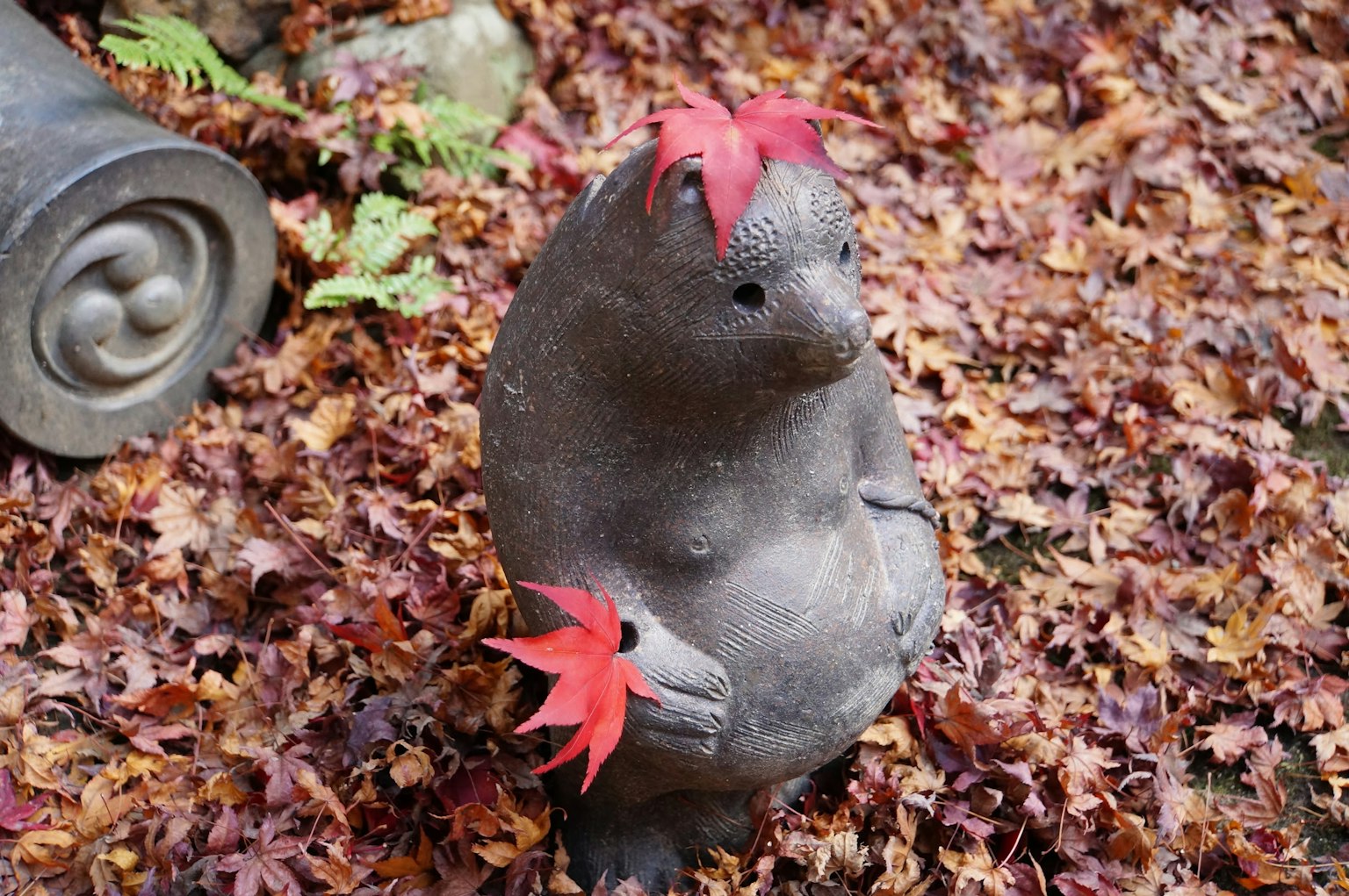 Escultura de oso de piedra sosteniendo hojas rojas rodeada de hojas de otoño