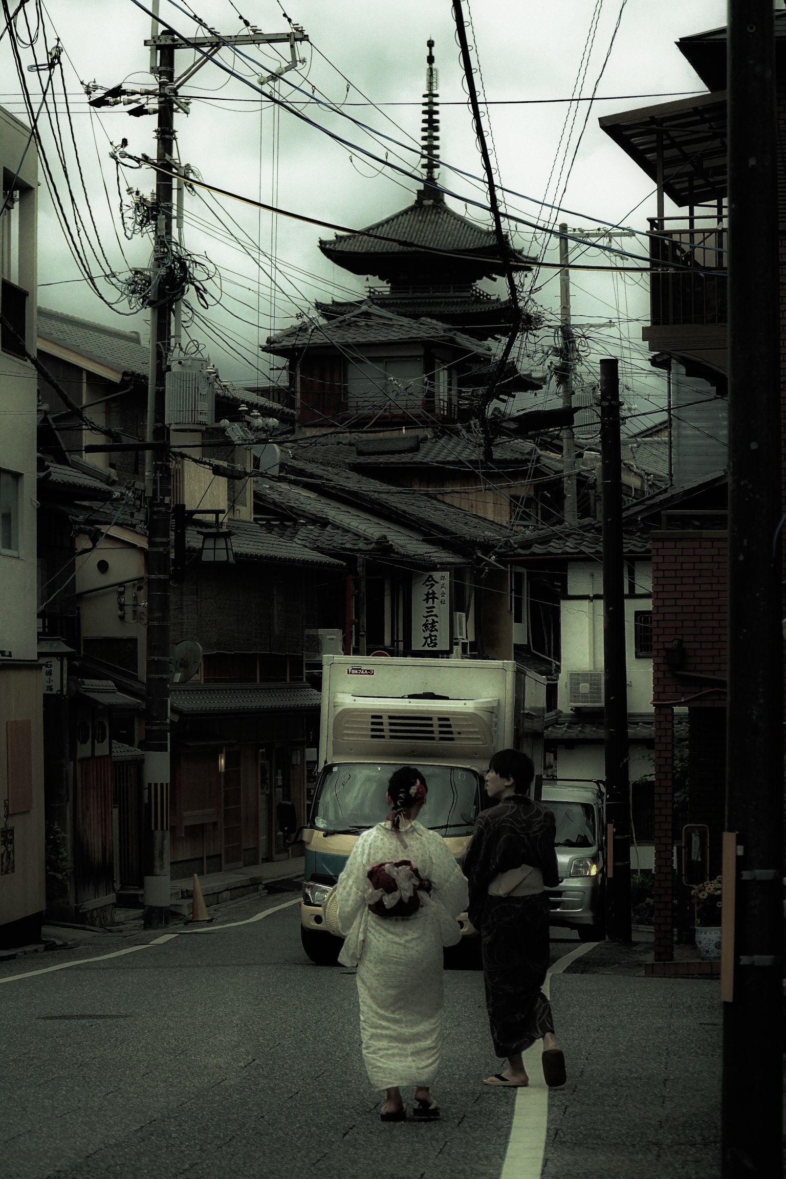 A woman in a kimono walking through a street with traditional buildings and power lines