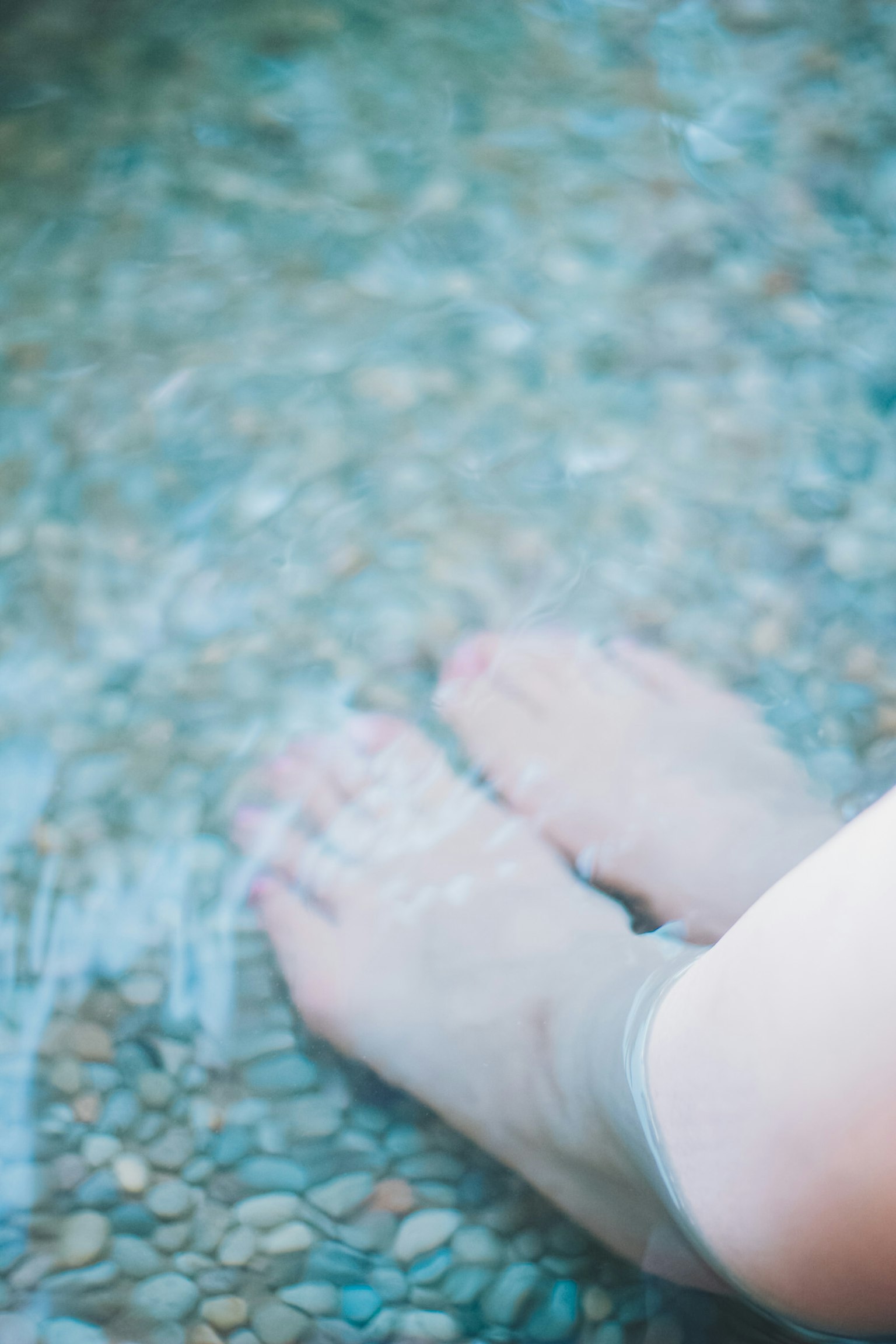 Füße im Wasser mit Kieselsteinen darunter