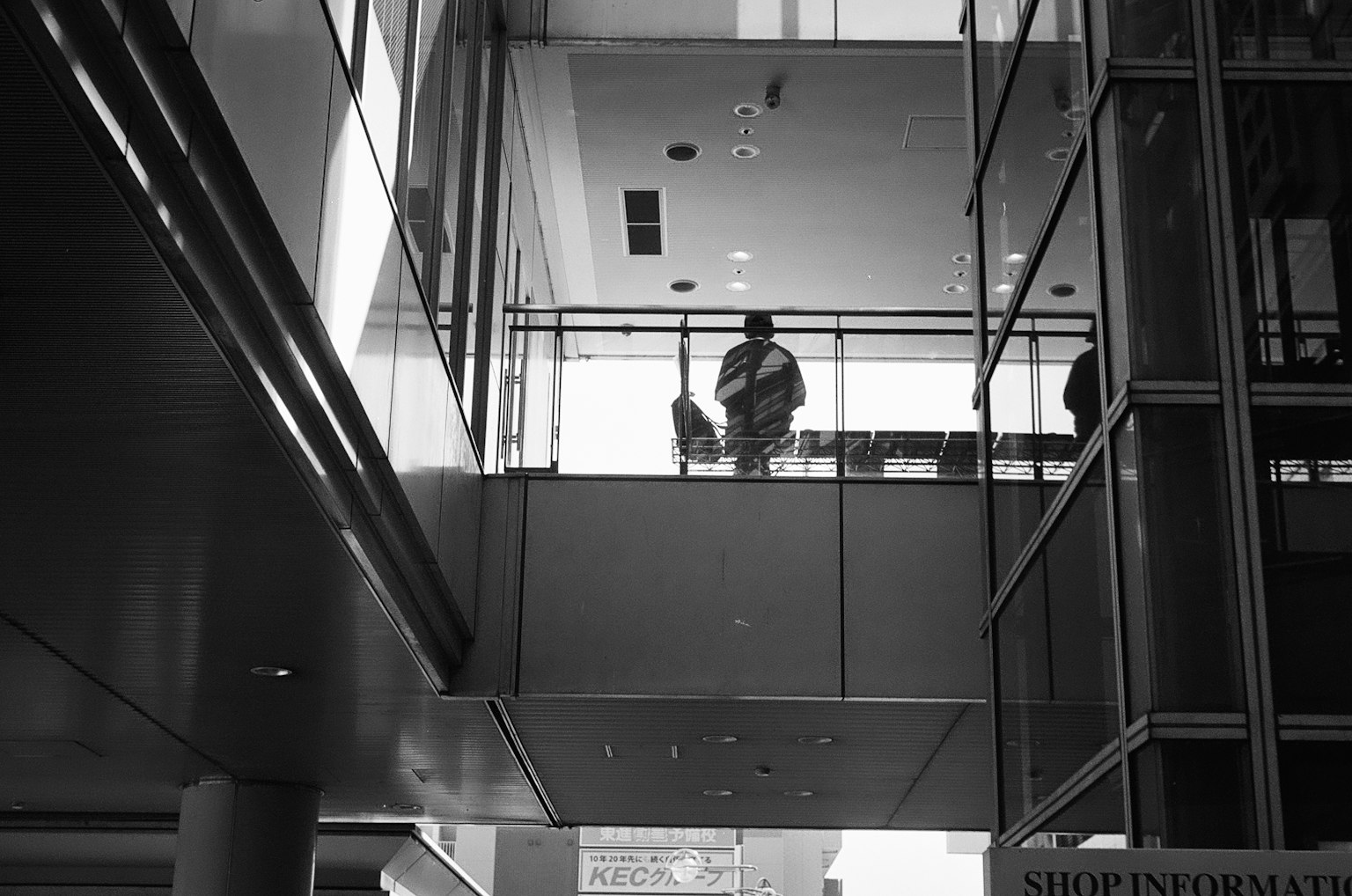 Foto hitam putih seseorang berdiri di balkon kaca dengan arsitektur modern dan pencahayaan