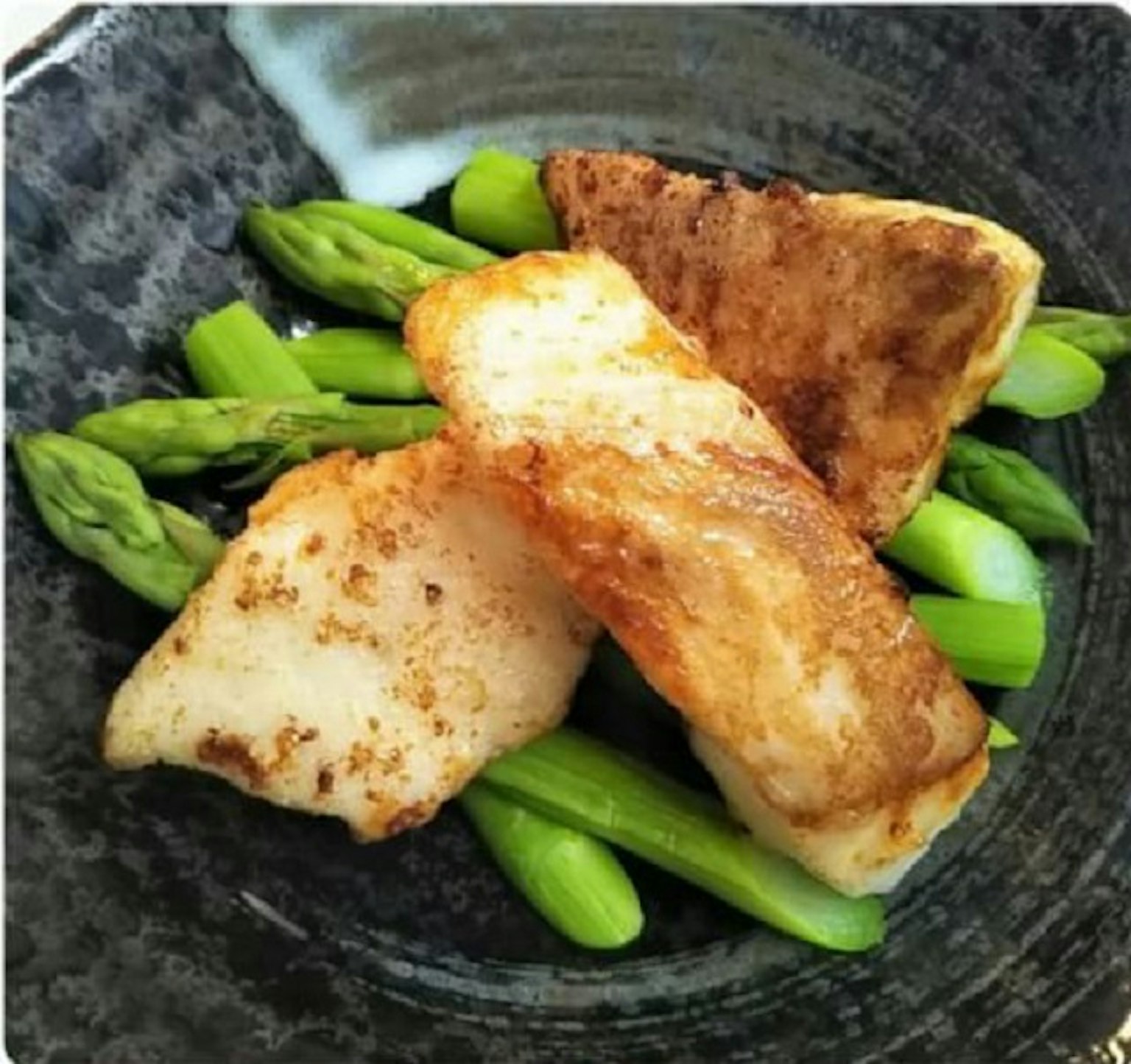 Poisson grillé servi sur une assiette noire avec des asperges