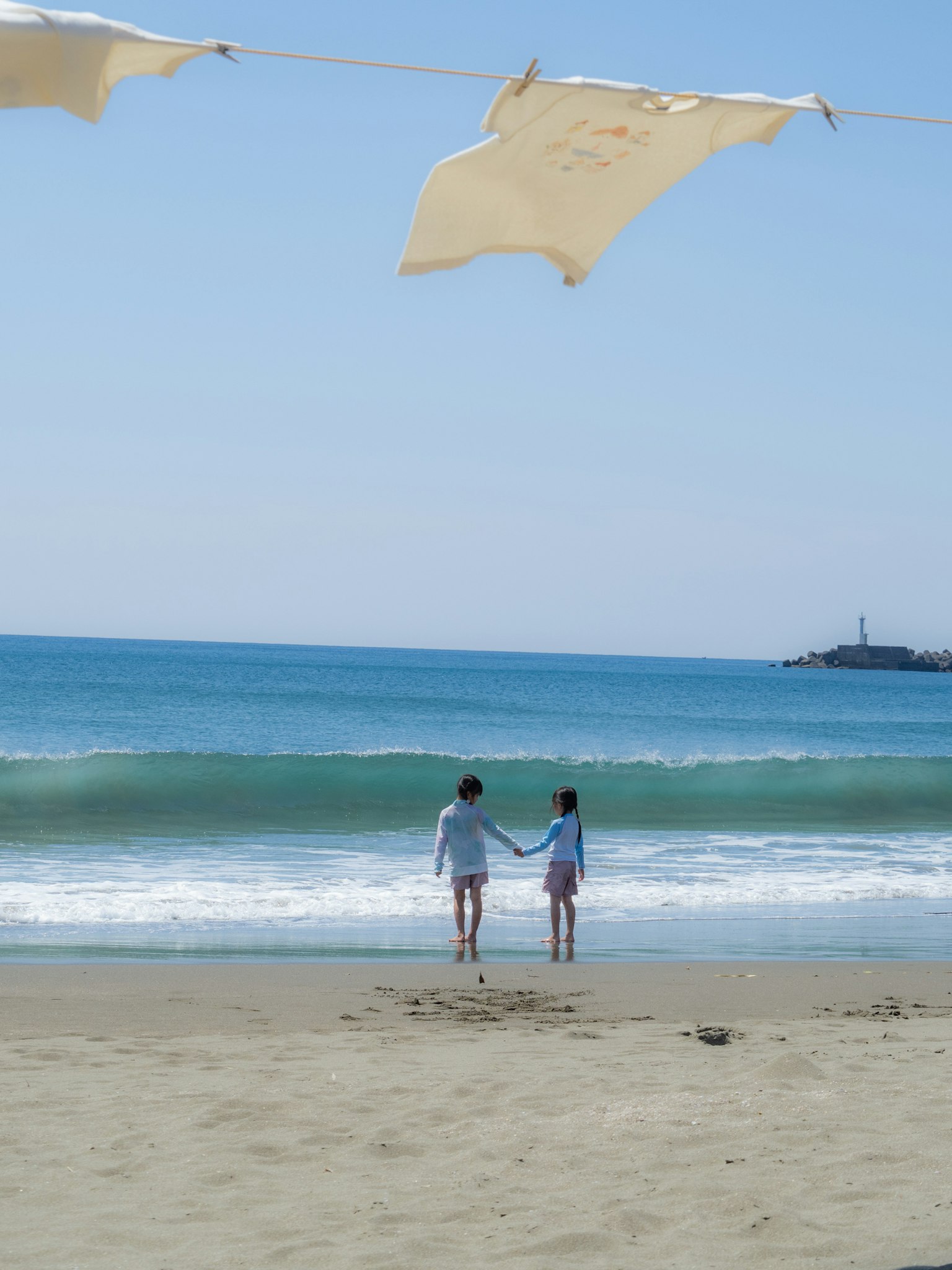 兩個孩子在海灘上手牽手，背景是藍色的海浪