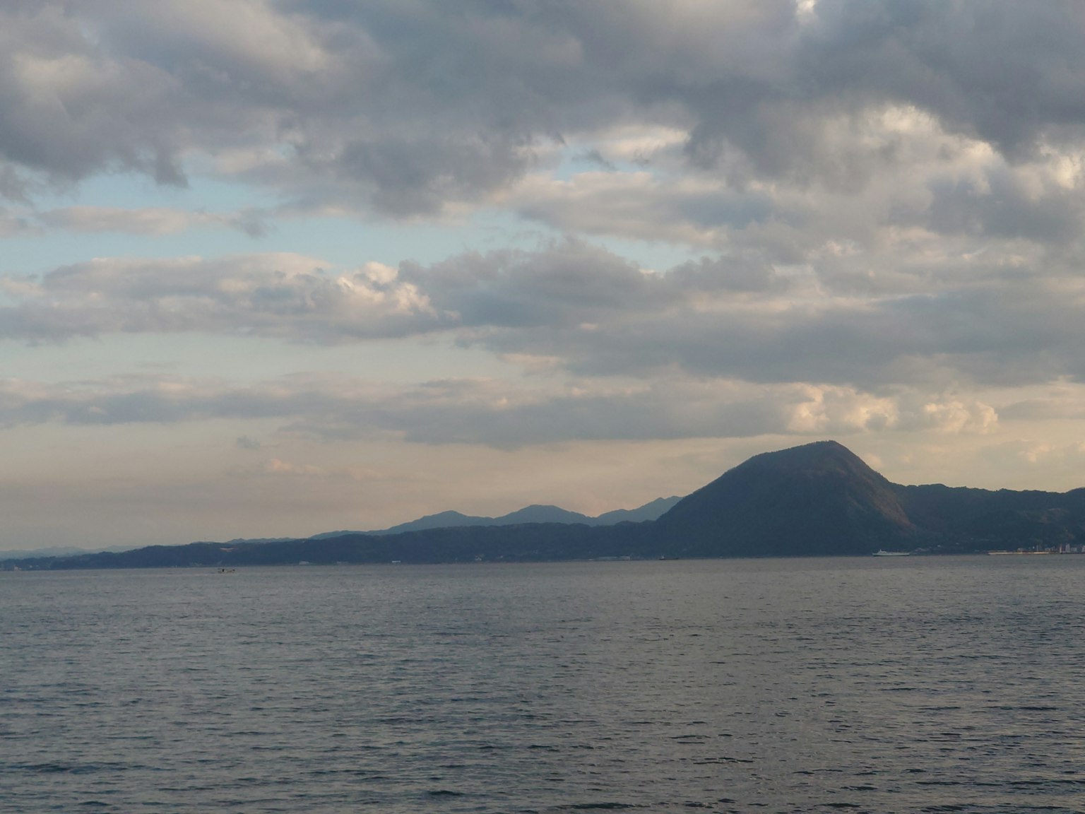 Landschaft mit Meer und Bergen unter bewölktem Himmel