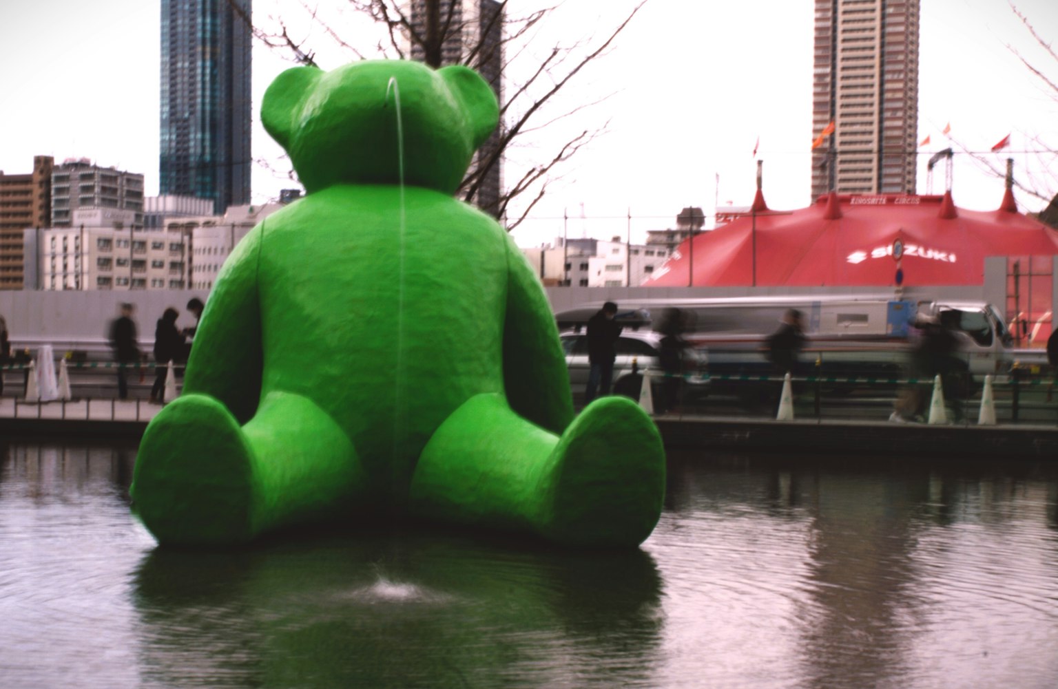 A large green bear sculpture sitting by the water with a city backdrop