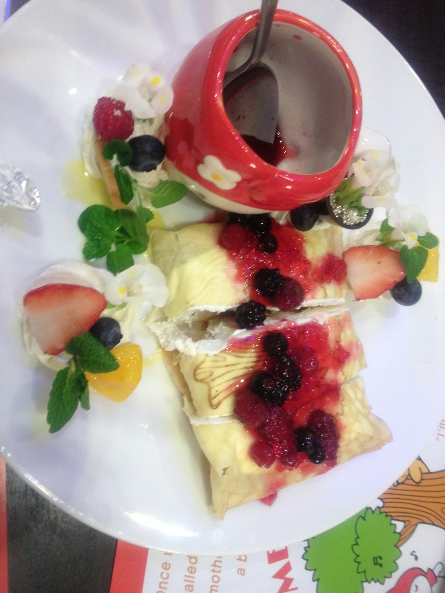 Piring dessert yang lezat dengan crepes krim custard ditambah saus beri mangkuk merah dengan saus cokelat