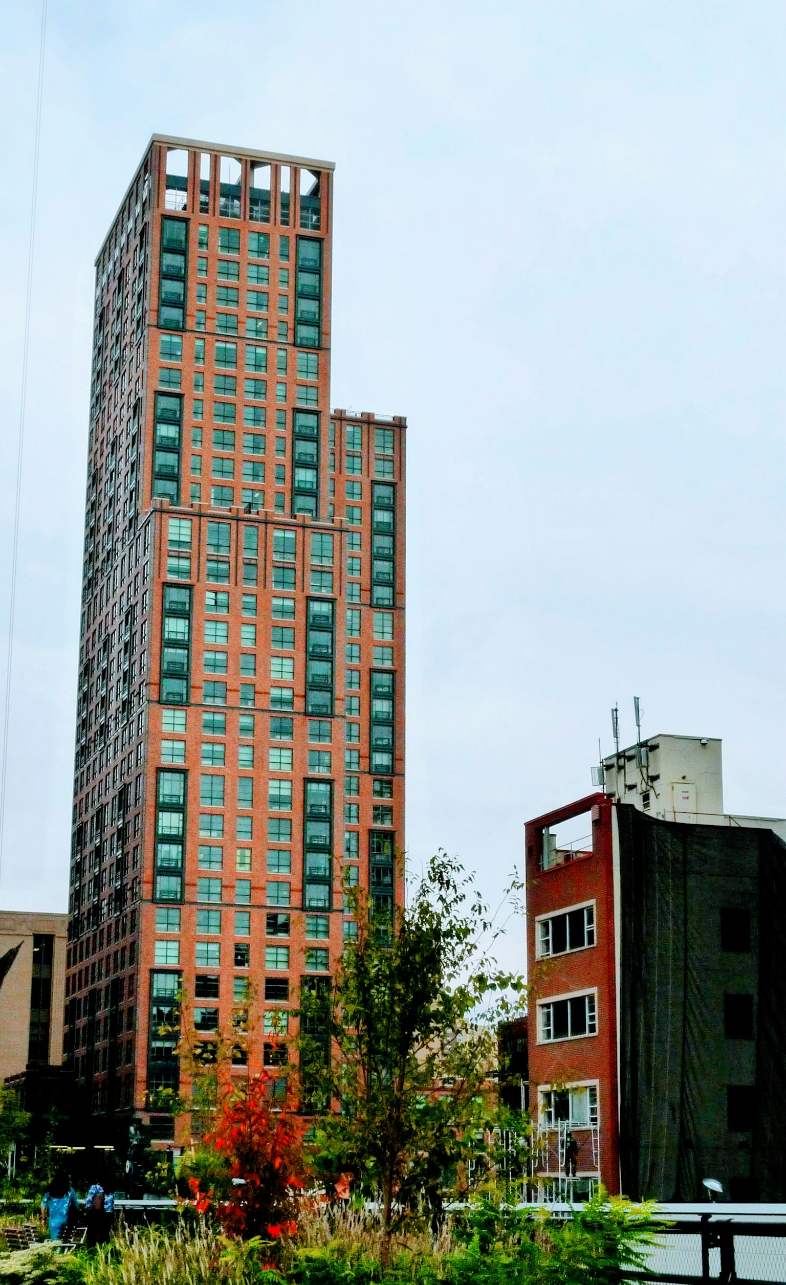 View of a tall building with modern architecture surrounded by smaller structures and greenery