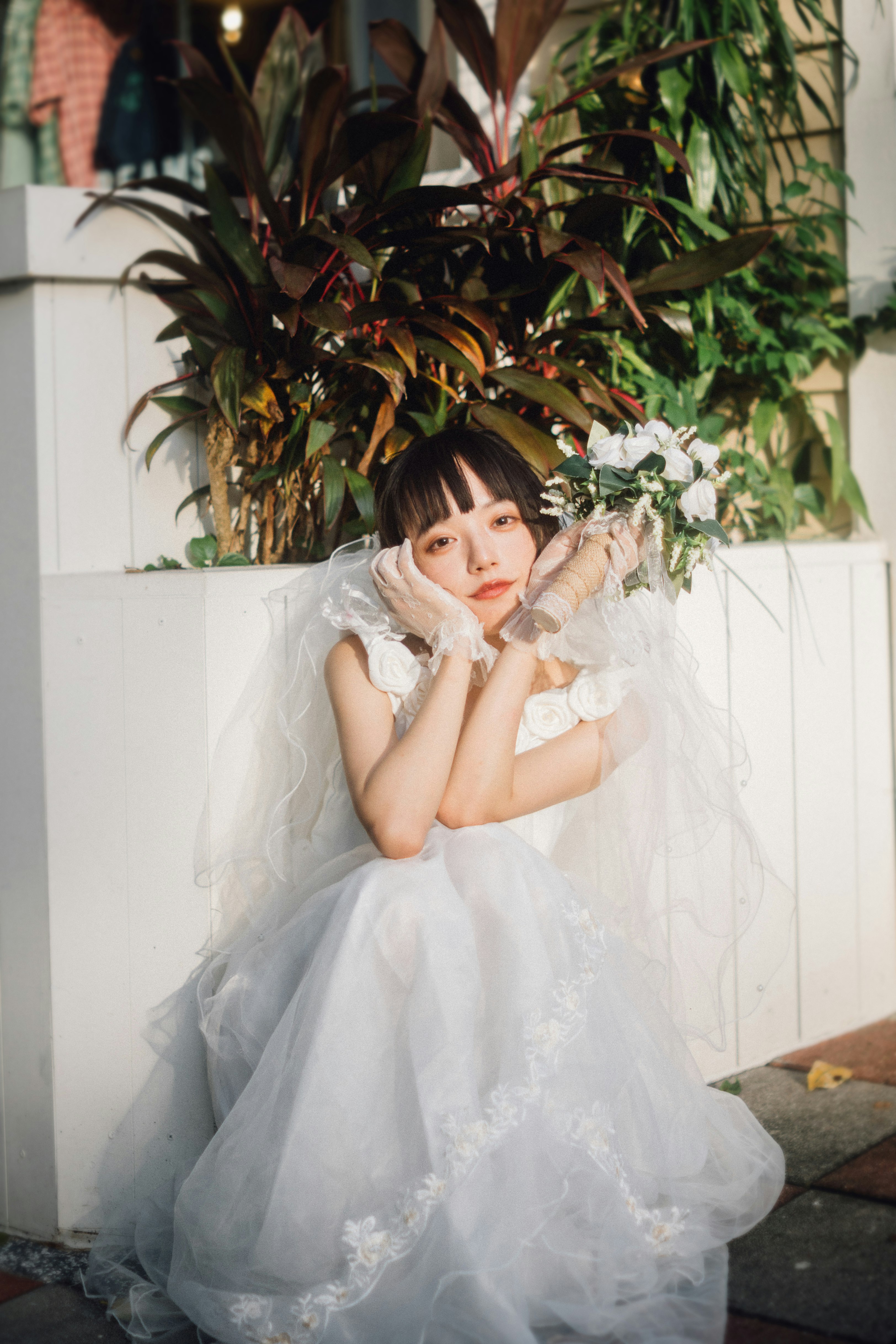 白いフリルのドレスをまとった少女が花飾りの前で微笑む