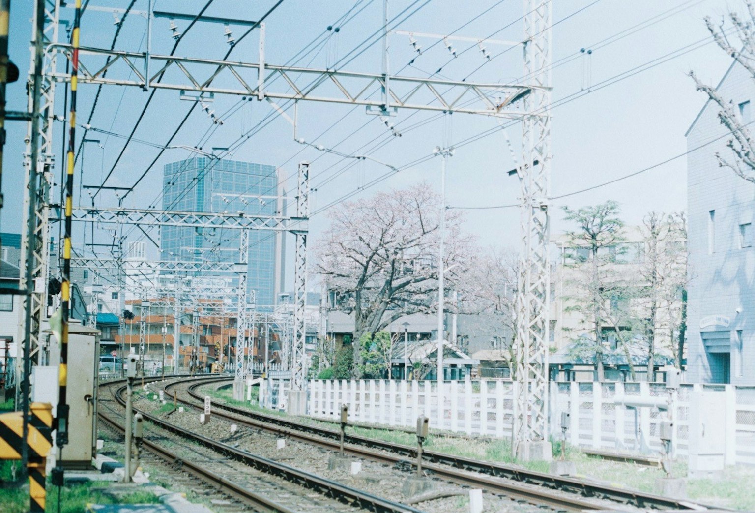 Vías de tren curvadas con edificios modernos y árboles de fondo