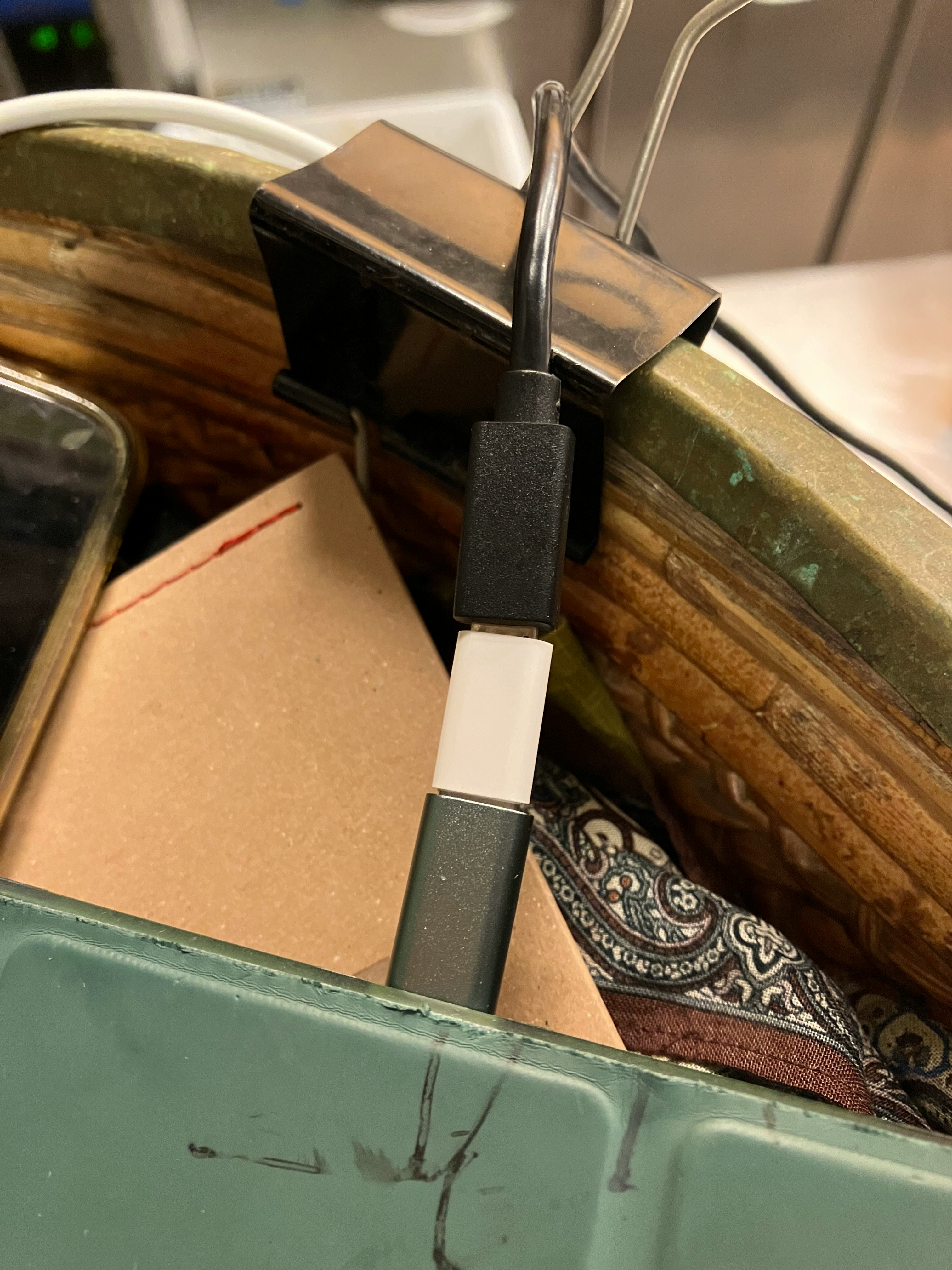Ein schwarzes Kabel und ein Clip sichtbar in einem Behälter voller verschiedener Gegenstände