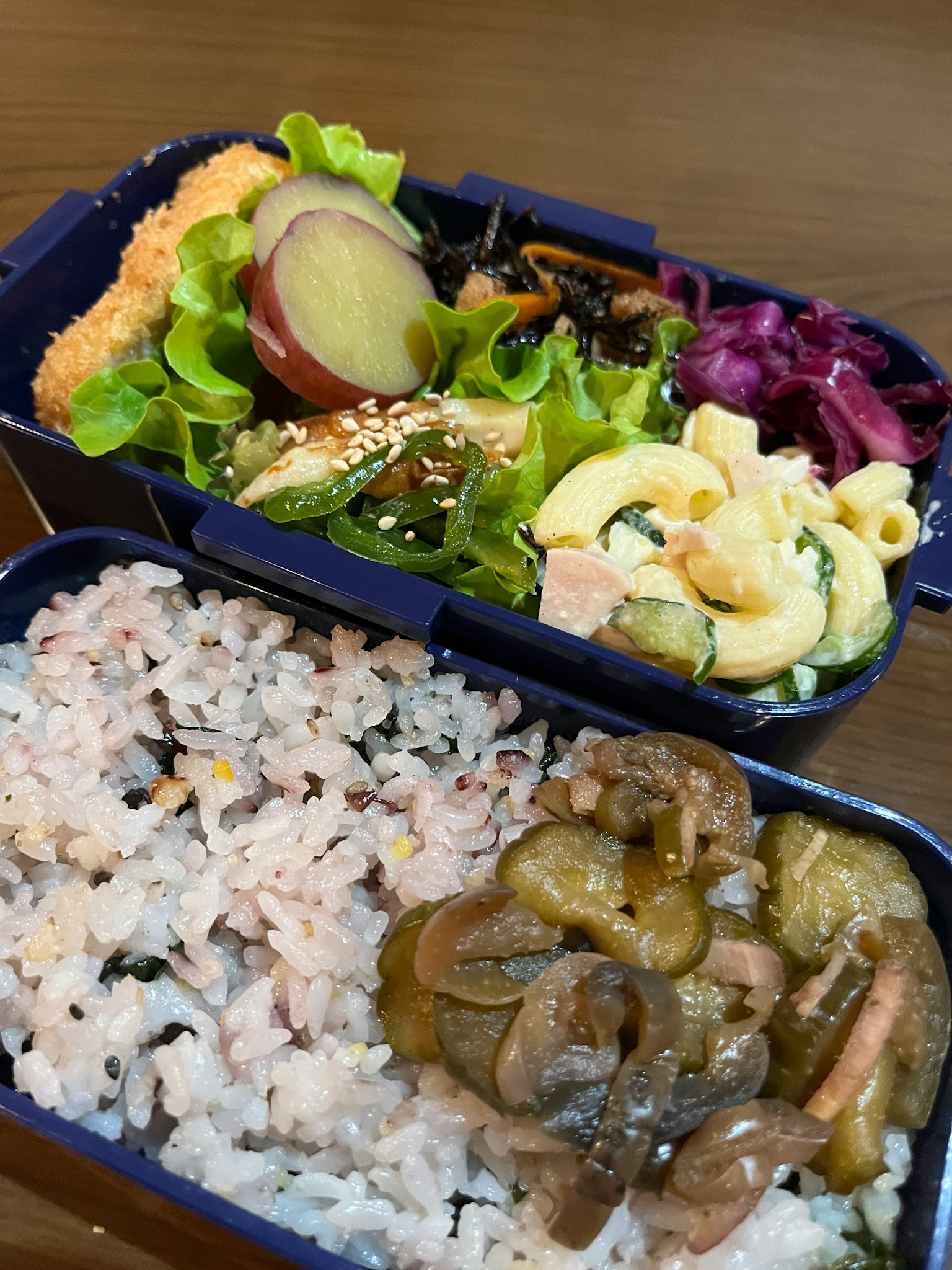 Hình ảnh hộp bento đầy màu sắc với salad và mì ống ở trên cơm và món ăn kèm ở dưới