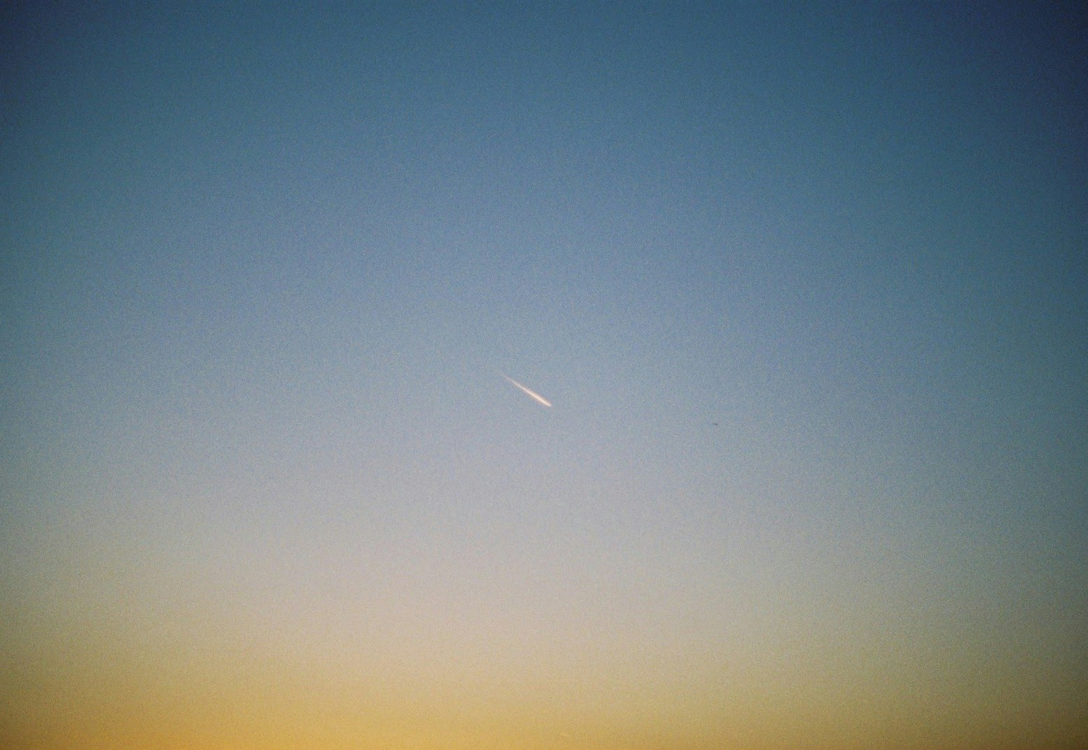 青空に伸びる細い流星のような光