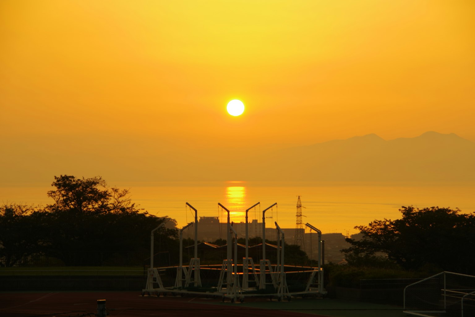 Tramonto che si riflette sul mare con silhouette di strutture sportive