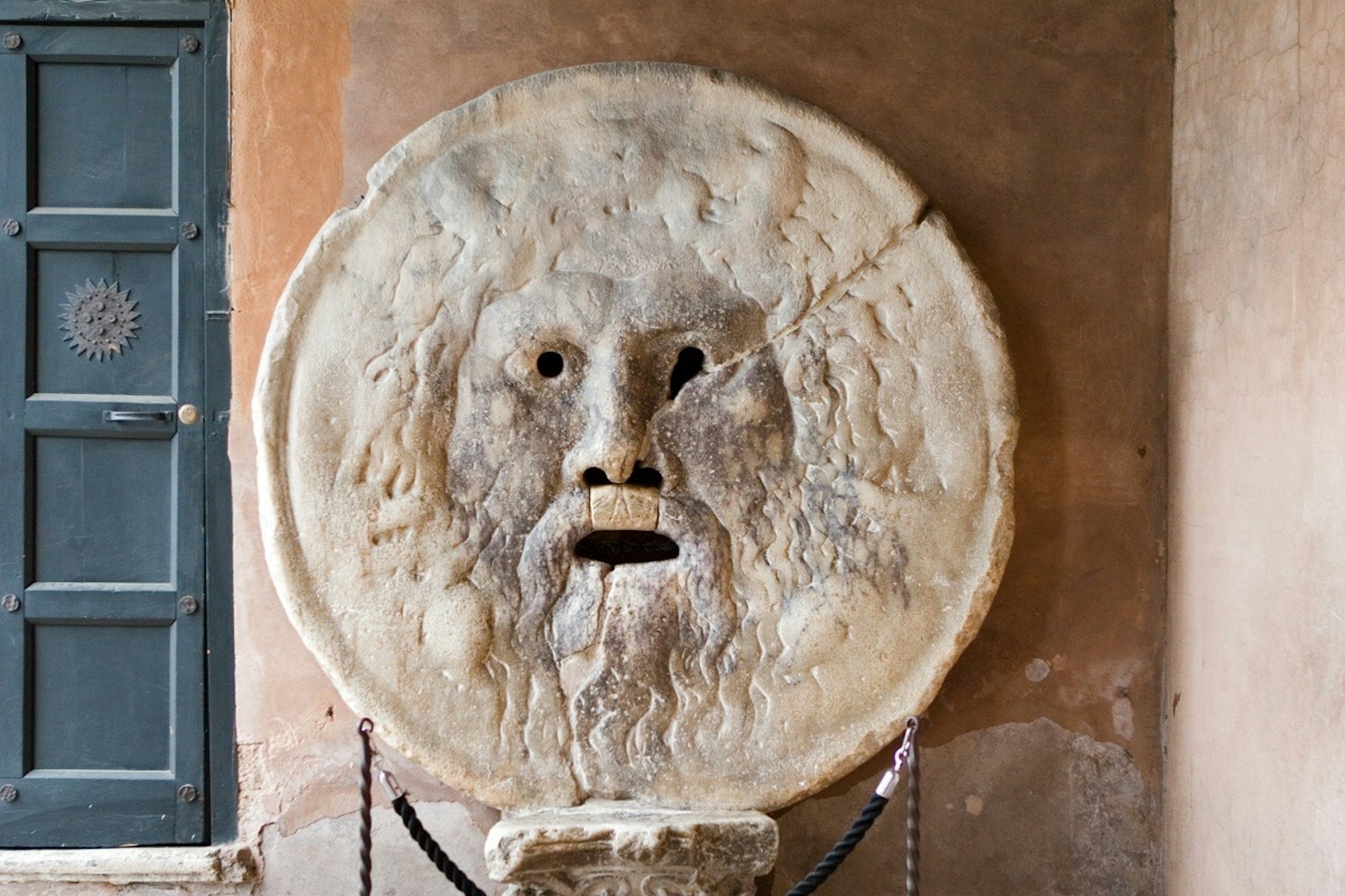 Escultura de piedra antigua de un rostro con boca abierta montada en una pared