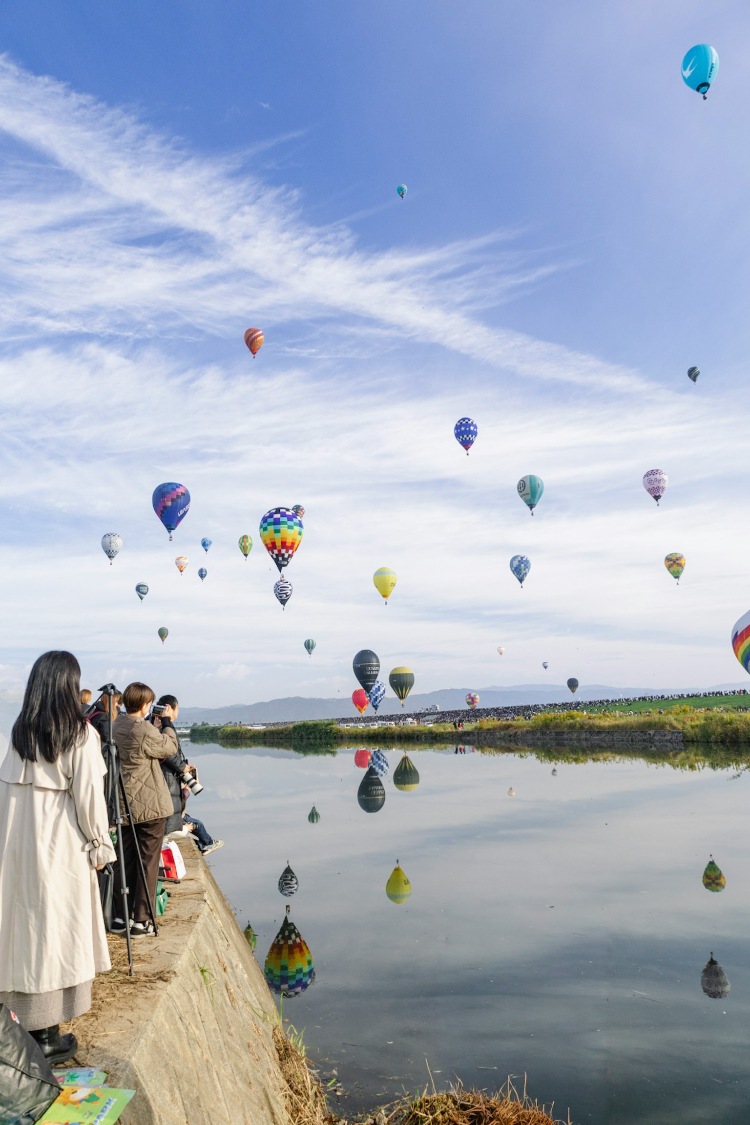 青空の下で熱気球が浮かぶ風景と川を見つめる人々