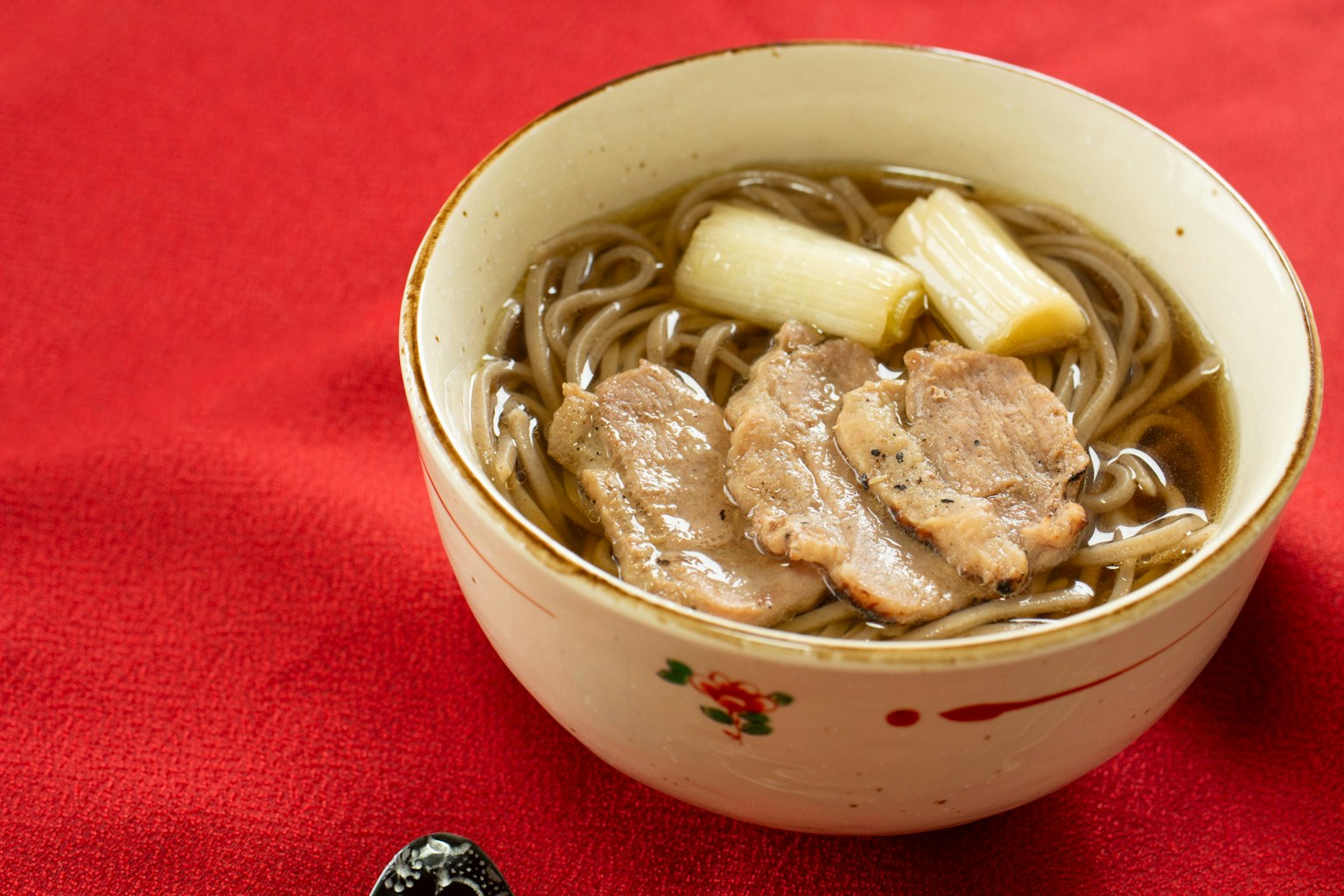 ชามบะหมี่โซบะที่มีหมูหั่นและต้นหอมบนพื้นหลังสีแดง