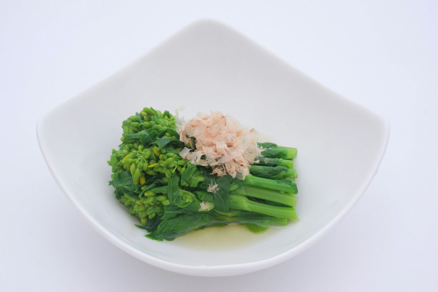Légumes verts garnis de flocons de poisson dans un plat blanc