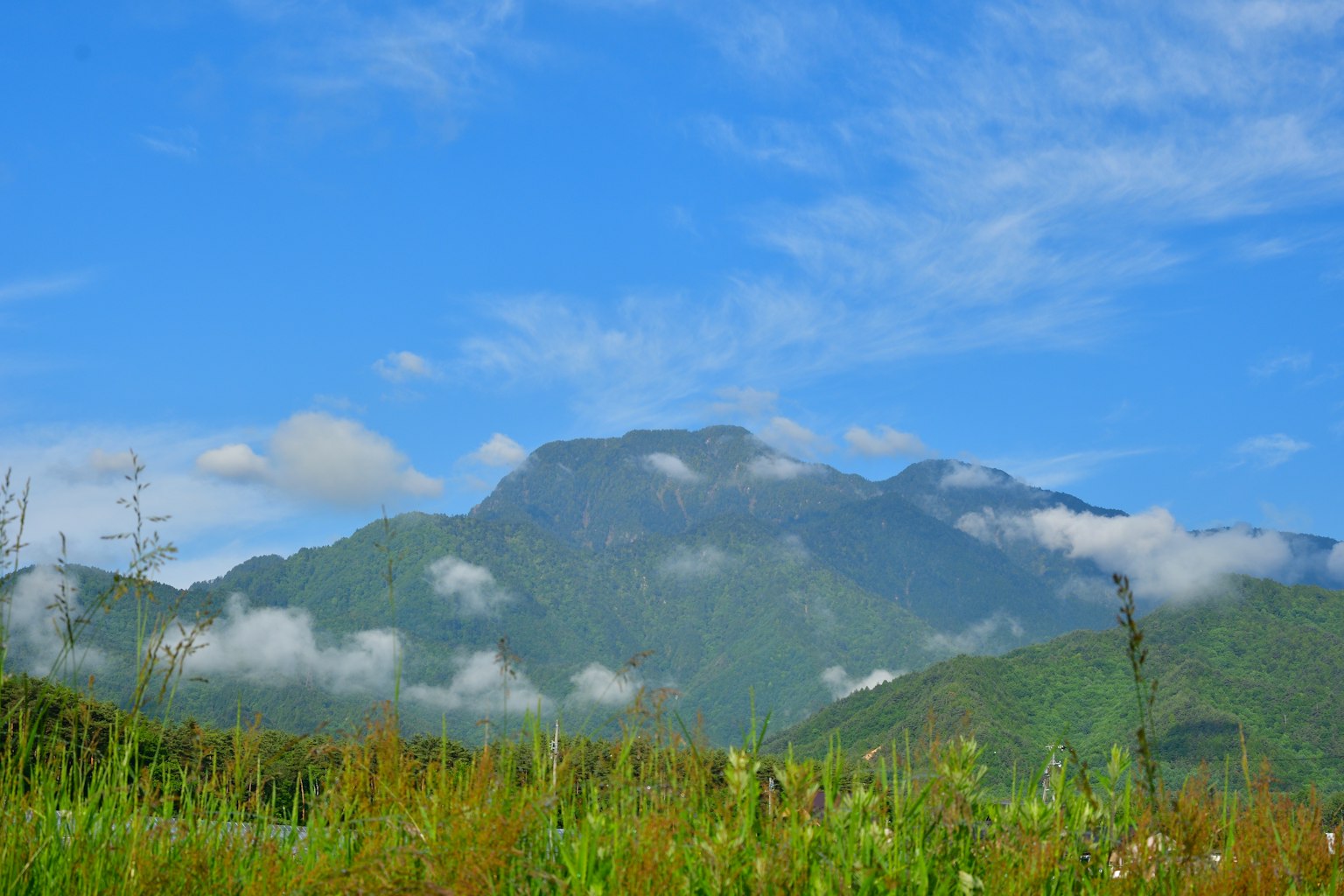 Vue panoramique d'une montagne verdoyante sous un ciel bleu avec des nuages