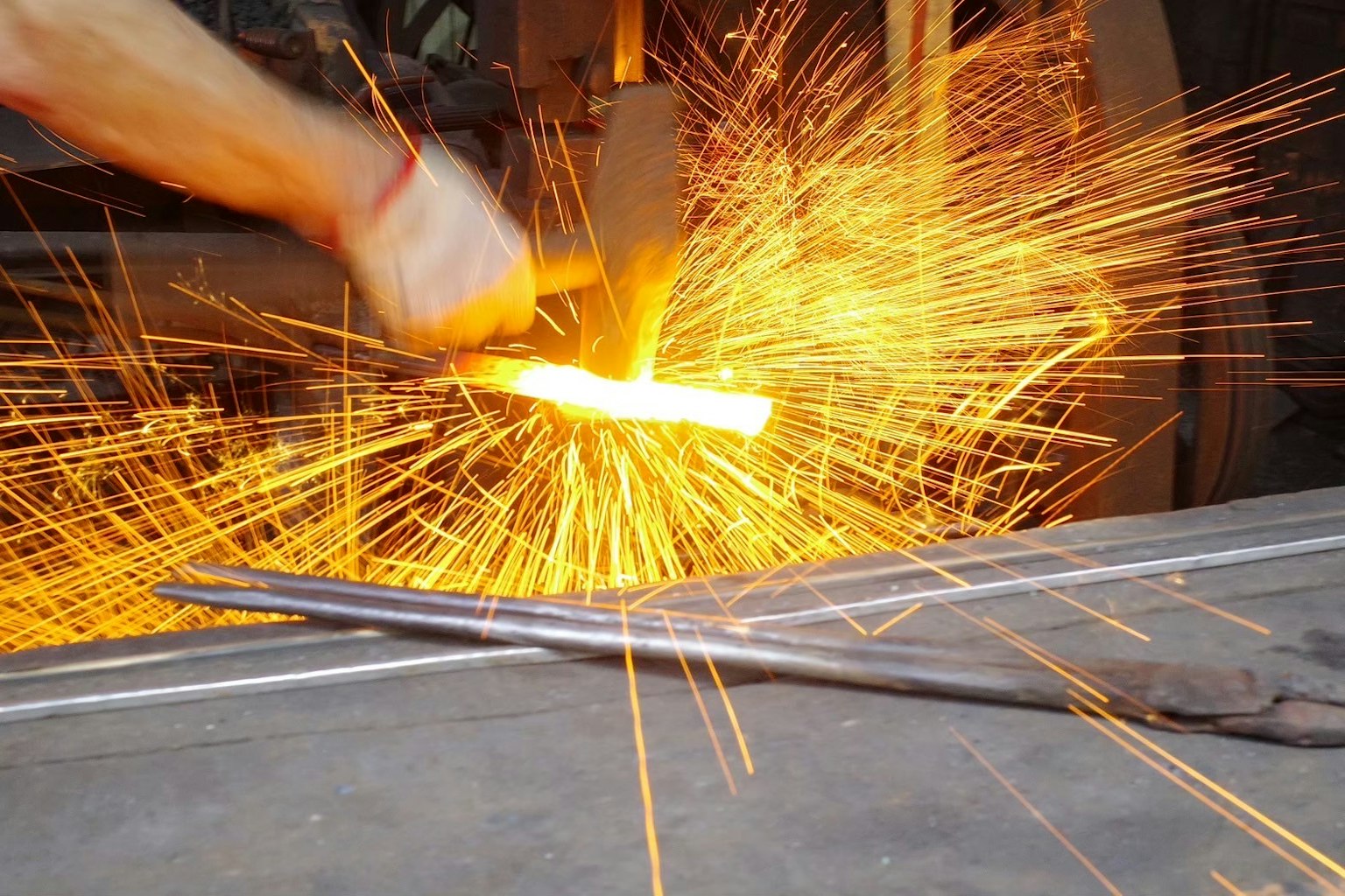 鍛冶作業中の火花が飛び散る様子 手に持った金属が赤く熱せられている