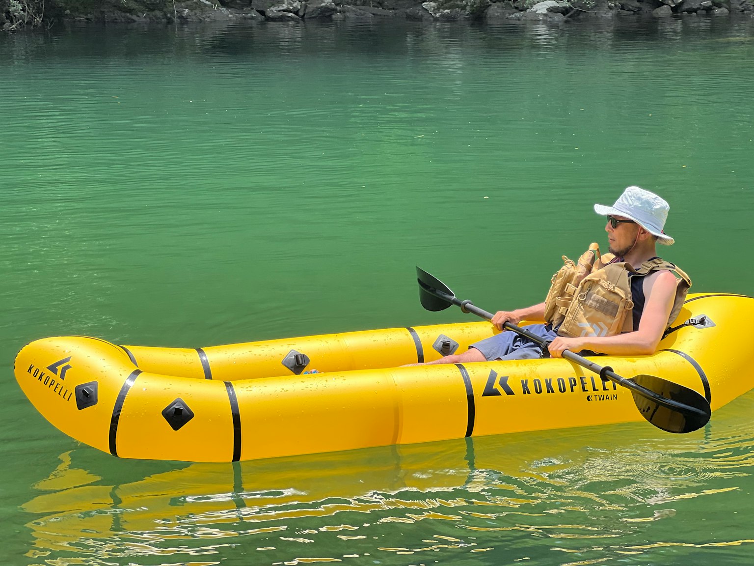 Ein Mann, der in einem leuchtend gelben aufblasbaren Kajak auf grünem Wasser paddelt