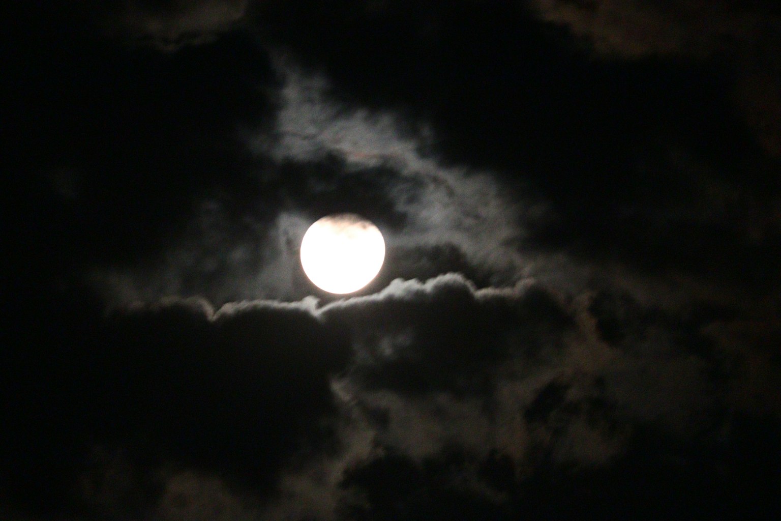 Bright full moon partially covered by clouds in a dark night sky