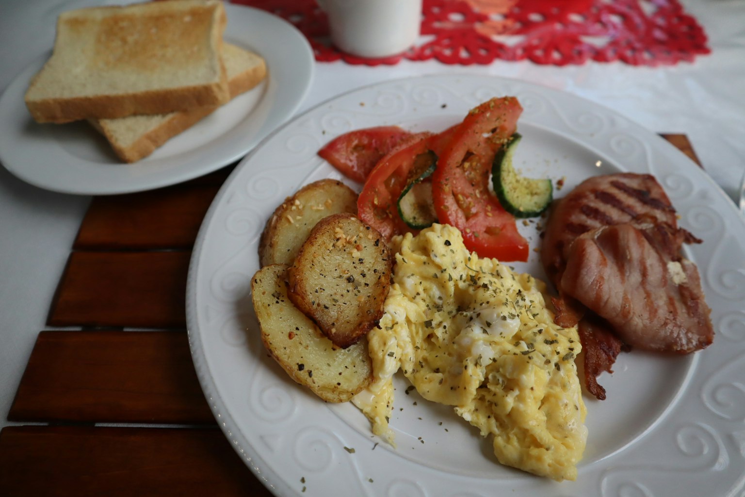 Plato de desayuno con huevos revueltos, papas, tomates, pepinos y jamón