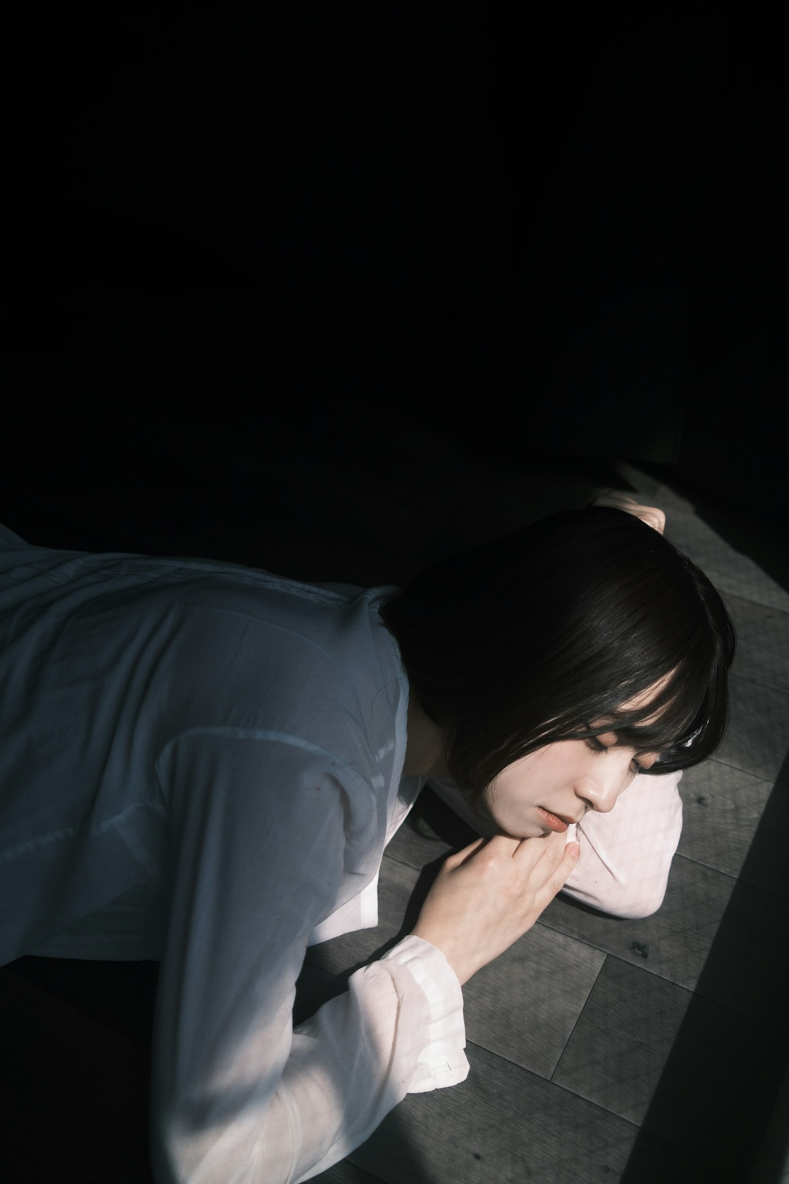 薄暗い部屋で横たわる女性の姿 白いシャツを着ている 光が彼女の顔に当たっている