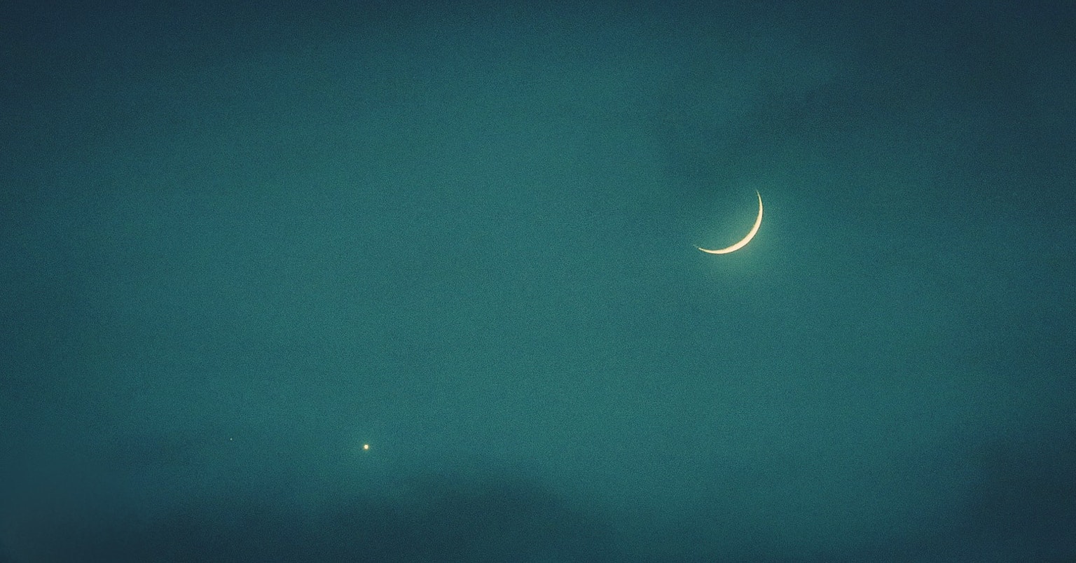 Luna crescente sottile e stella in un cielo notturno blu