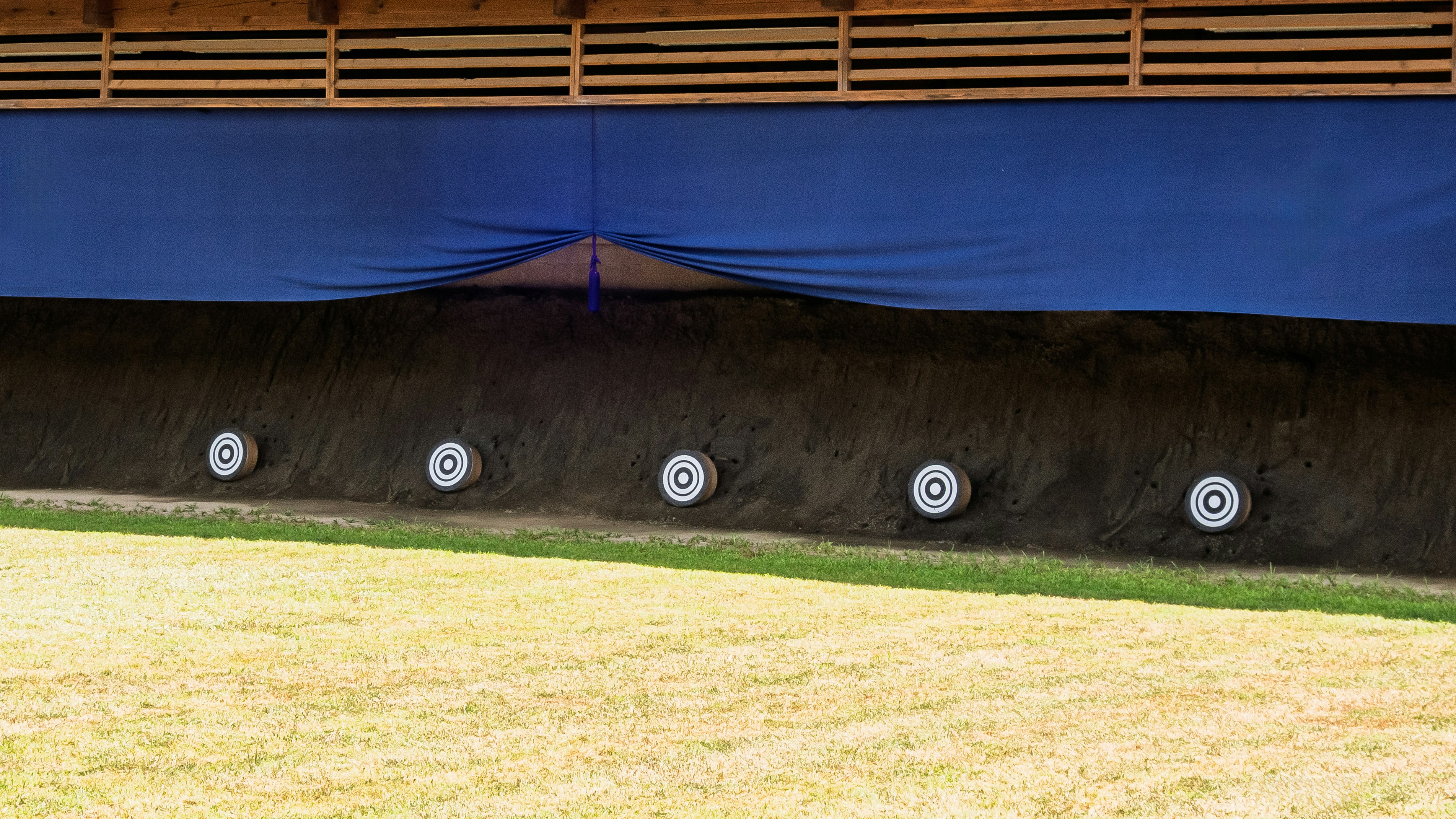 outdoor shooting range with targets and a blue tent over grass