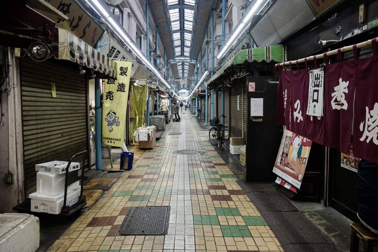 Calle vacía de una estrecha calle comercial con persianas cerradas y baldosas coloridas