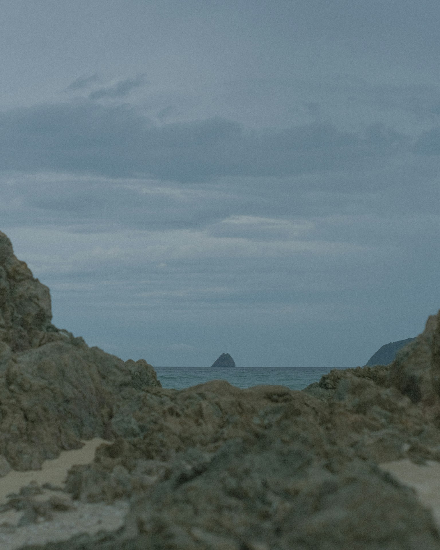 Paisaje marino con rocas bajo un cielo nublado y una isla a lo lejos