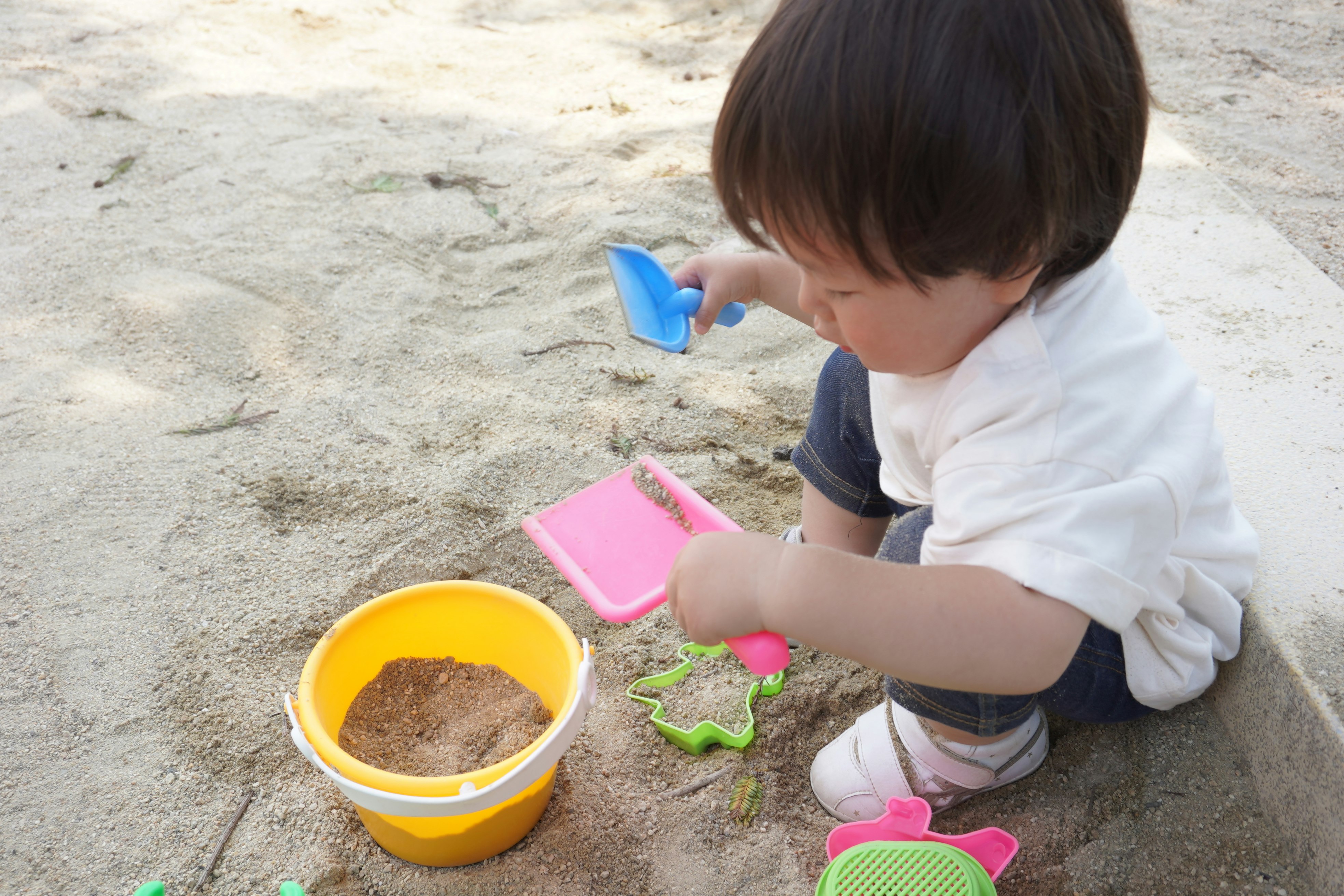 enfant jouant dans un bac à sable avec des jouets et un seau