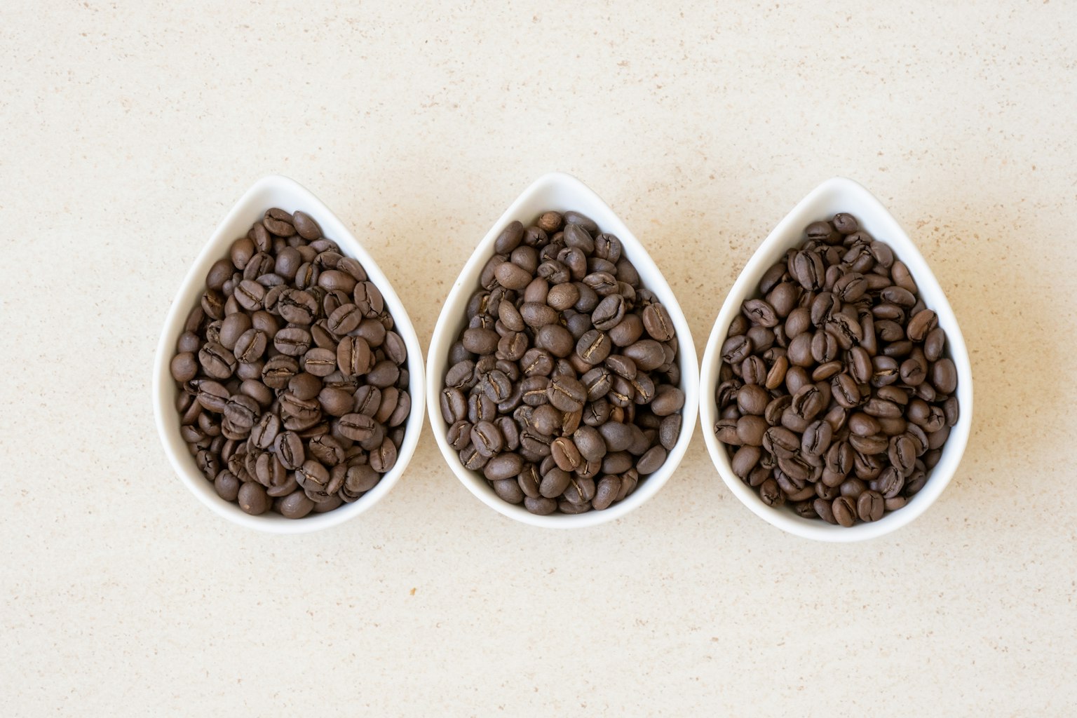 Image de grains de café dans trois plats en forme de goutte blancs