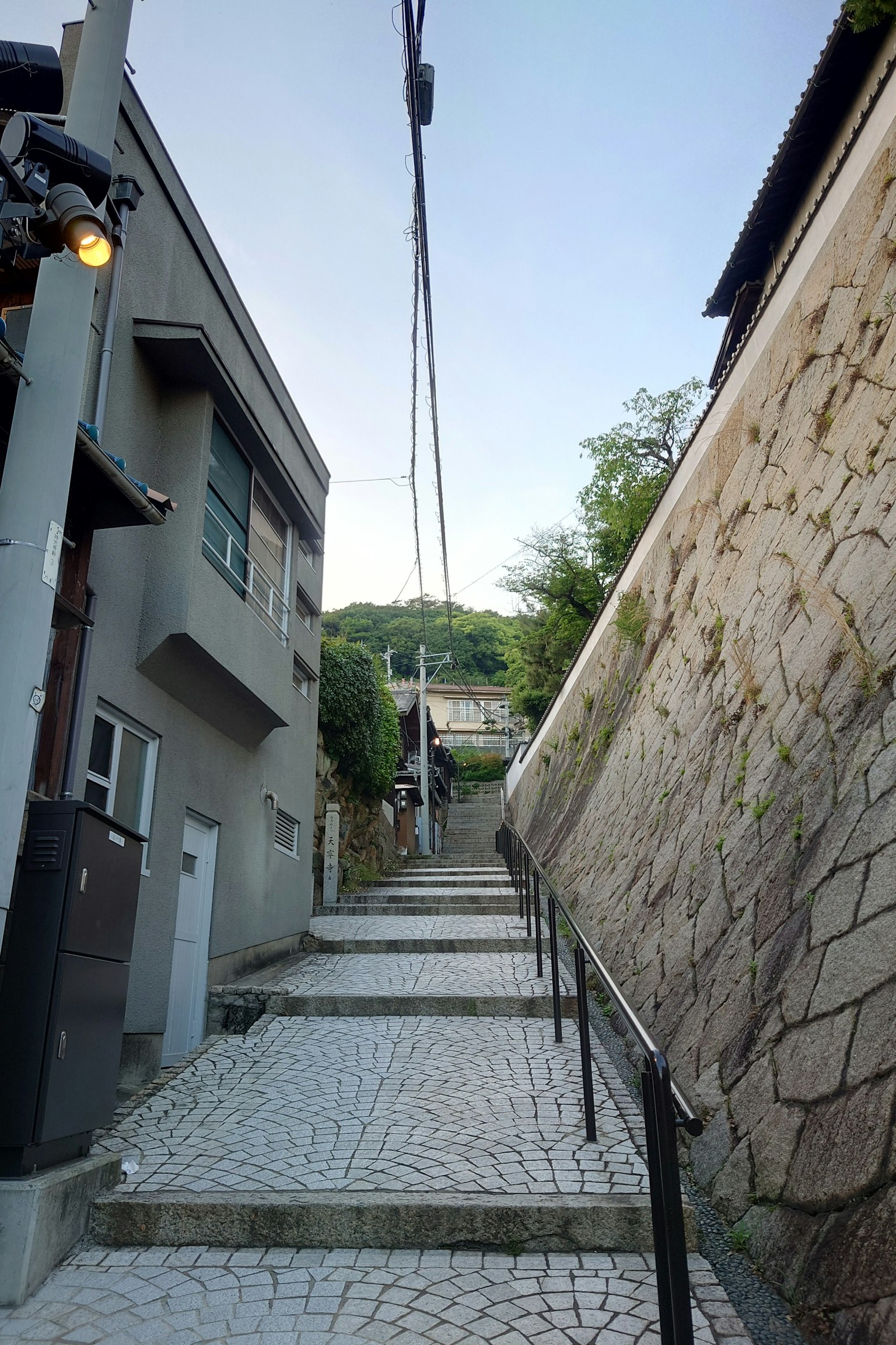 Strada stretta con muro di pietra e scale che portano in alto