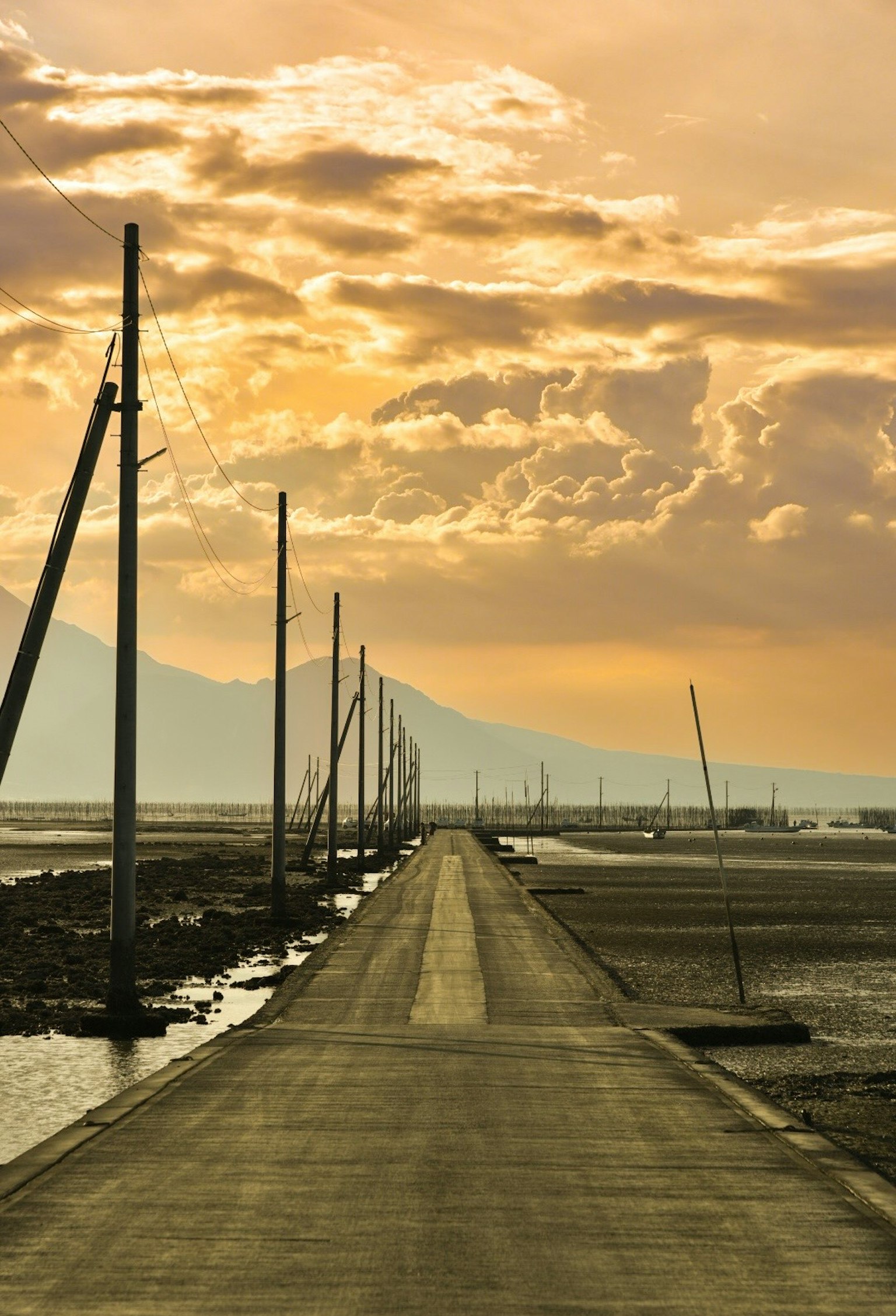 Strada asfaltata fiancheggiata da pali sotto un cielo al tramonto