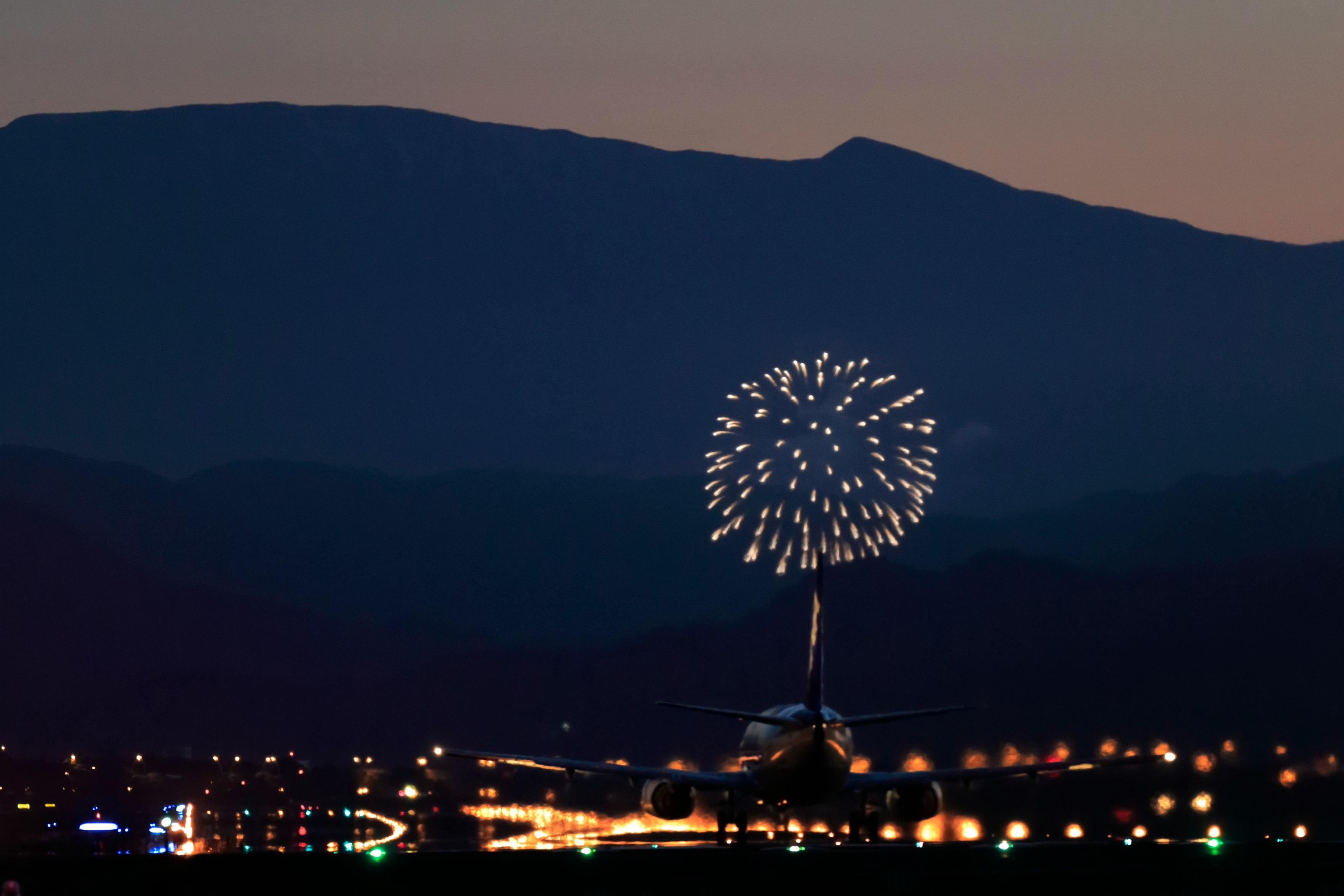 山並みを背景に打ち上がる花火と夜景の光