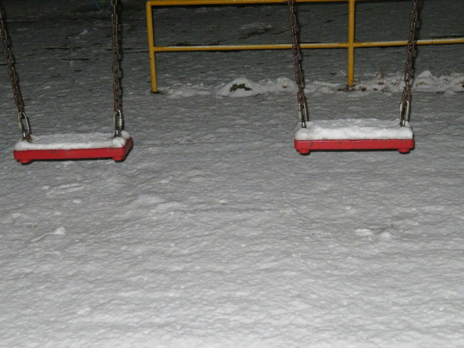 Zwei rote Schaukeln auf schneebedecktem Boden mit einem gelben Rahmen
